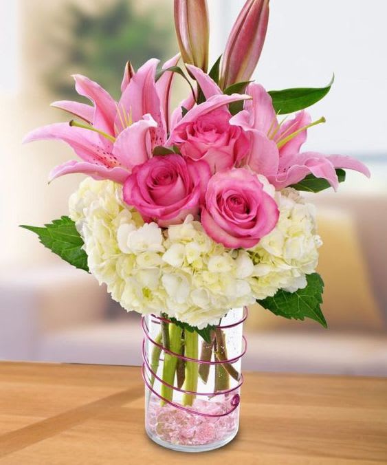 Pink lilies and roses arranged with white hydrangeas in a glass vase