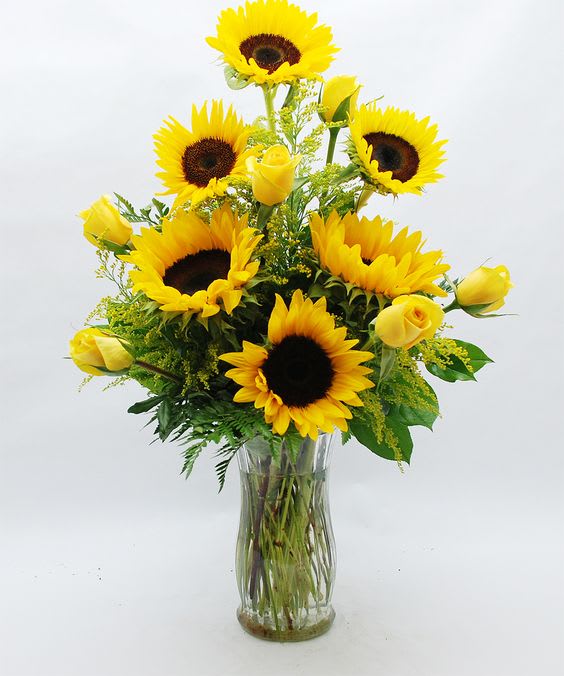 Sunflowers and yellow roses arranged in a clear glass vase