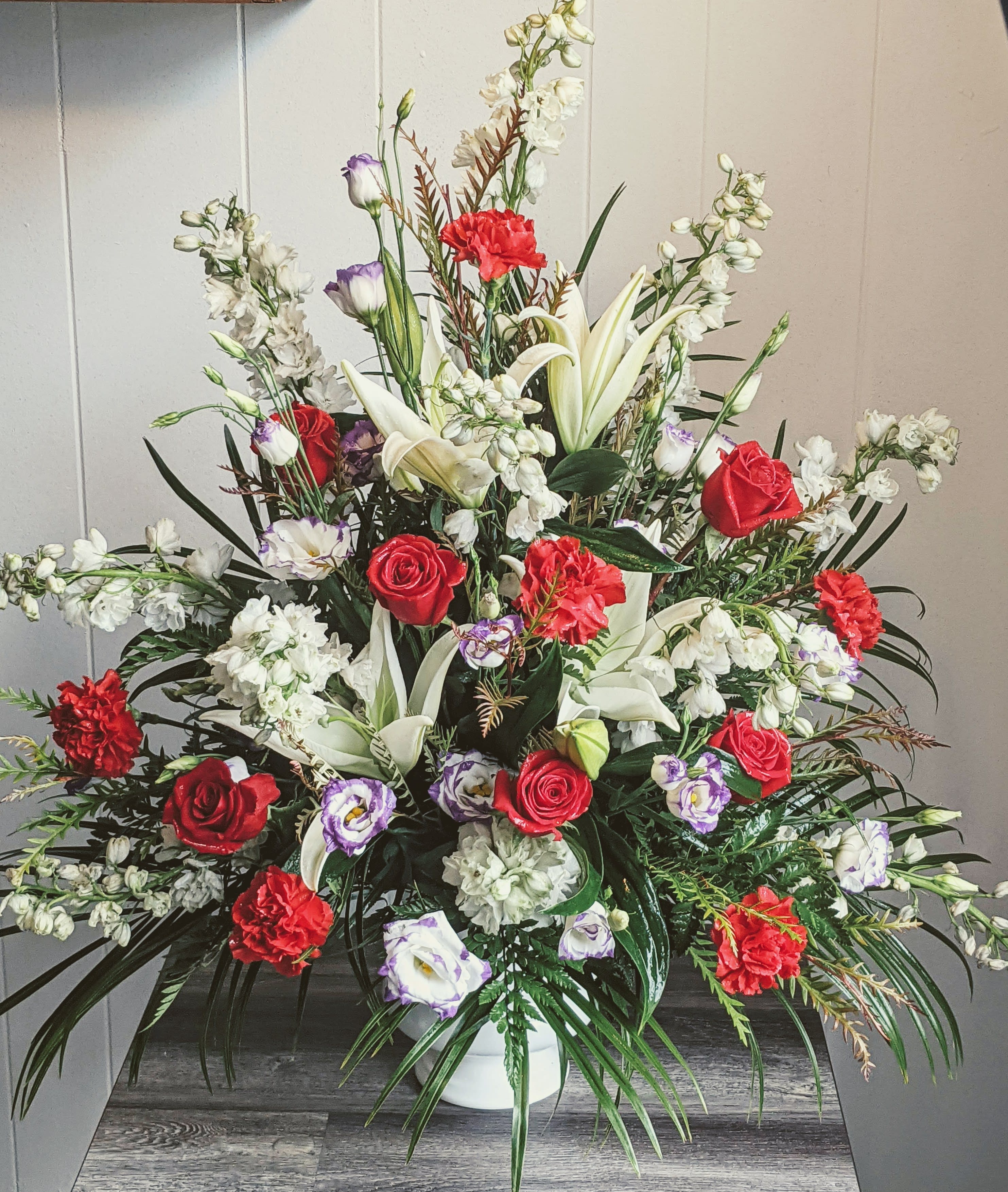 Large mixed floral arrangement with red roses, white lilies, and white blossoms in a vase