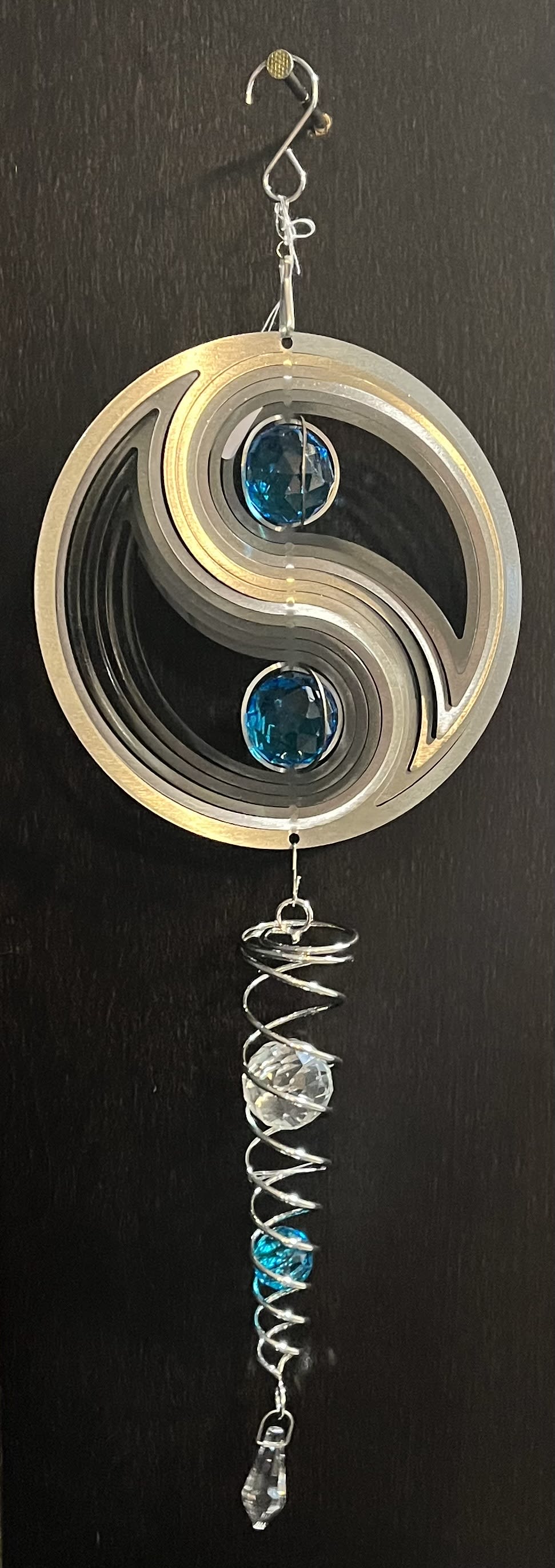 Metal wind chime with blue and clear crystal accents hanging on a dark surface