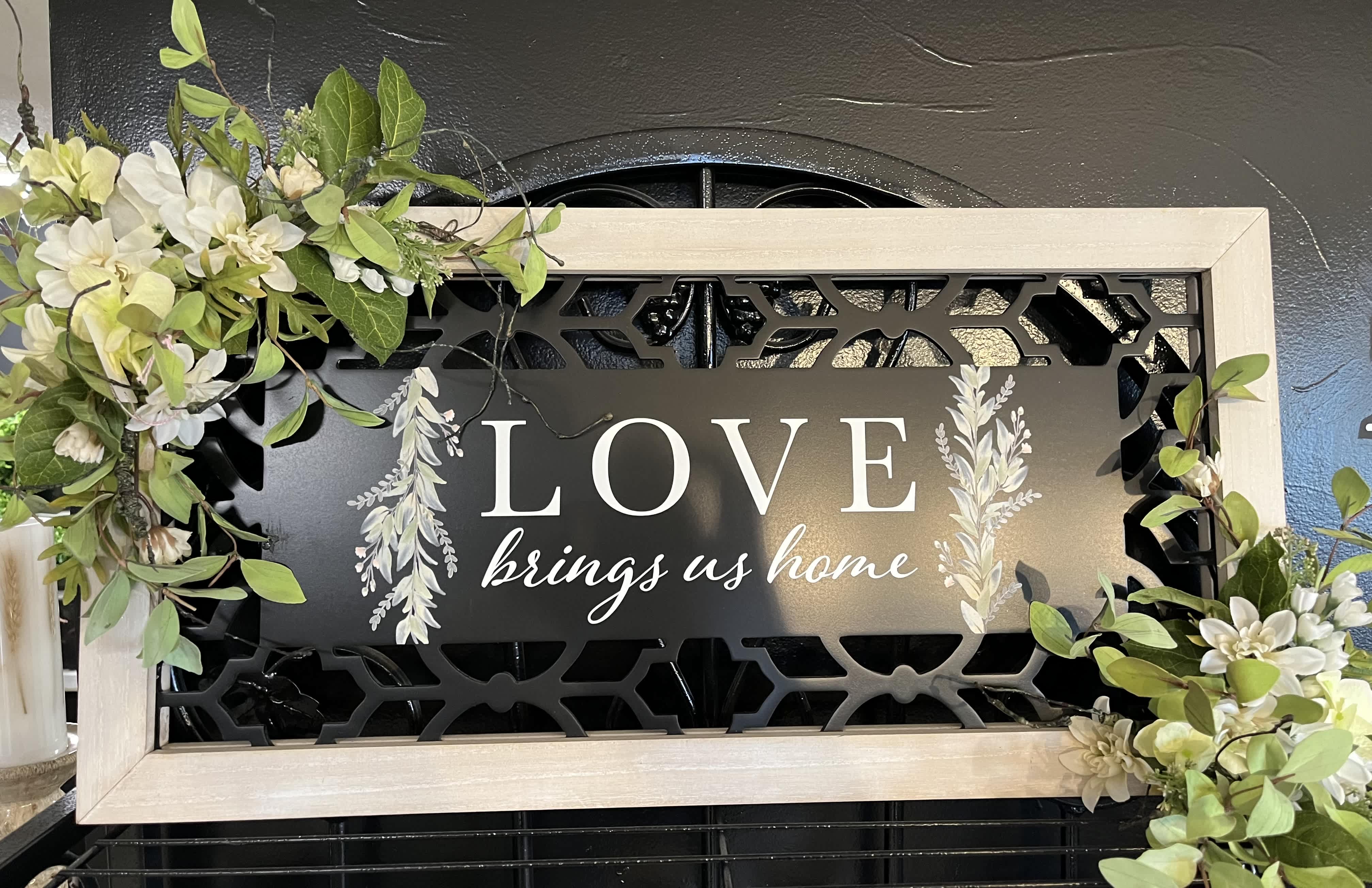 Framed sign with white floral accents and the words "LOVE brings us home"