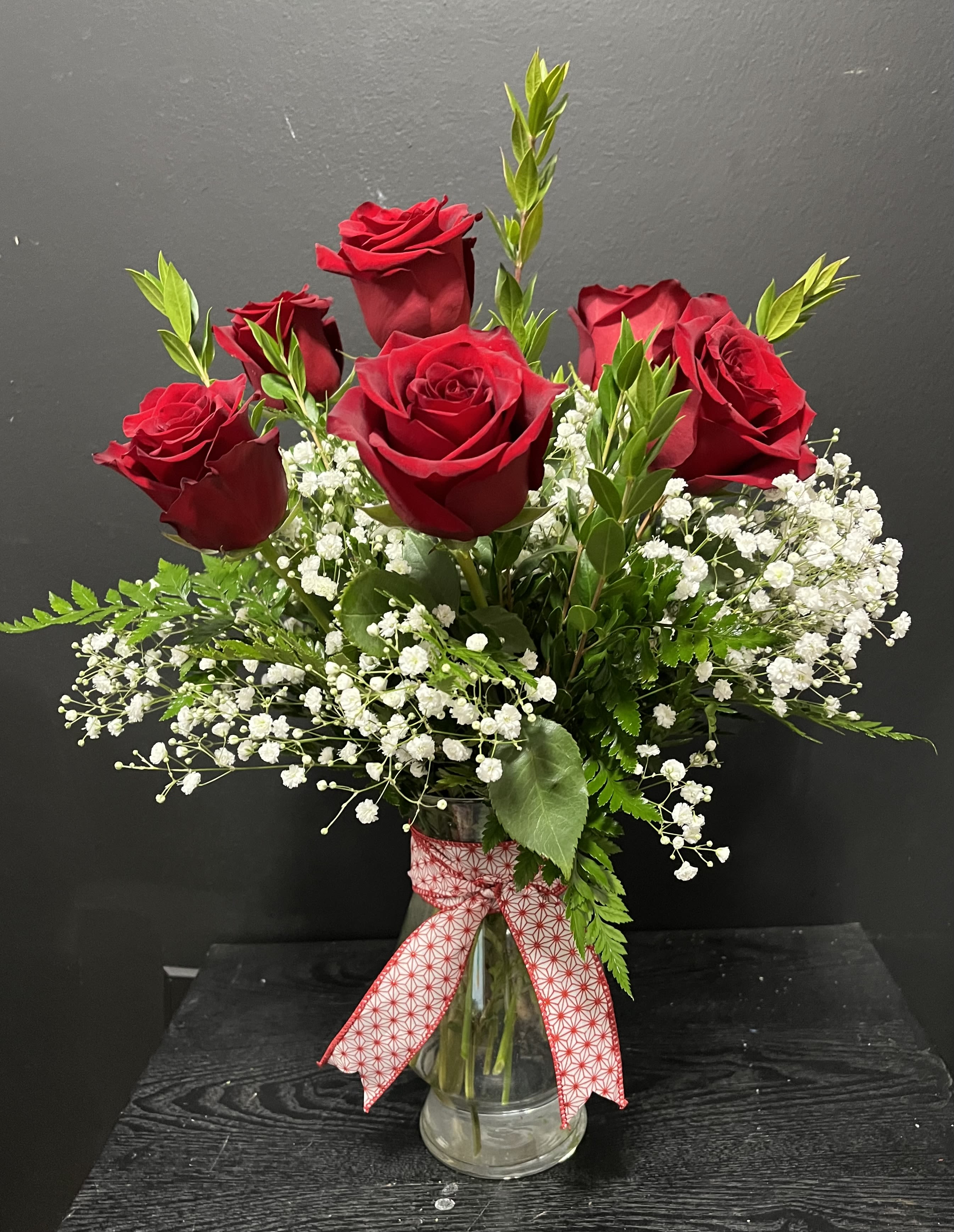 Red roses in a clear glass vase with baby's breath and a ribbon