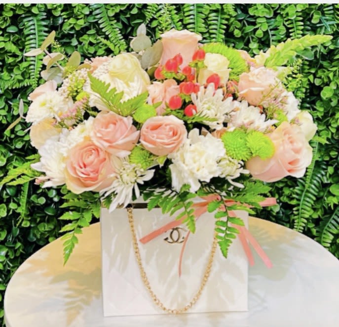 Pink and white rose arrangement in a white gift bag with ribbon