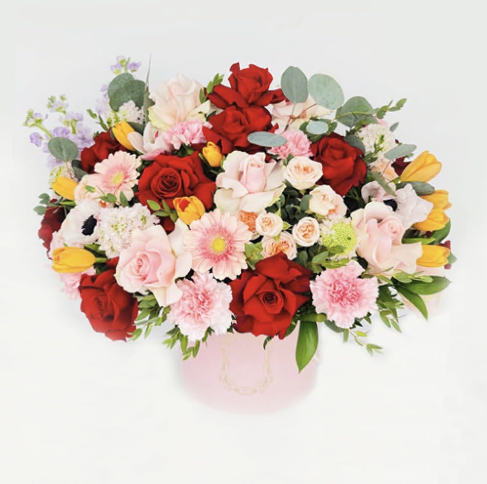 Mixed bouquet of red and pink roses with yellow tulips in a pink hatbox