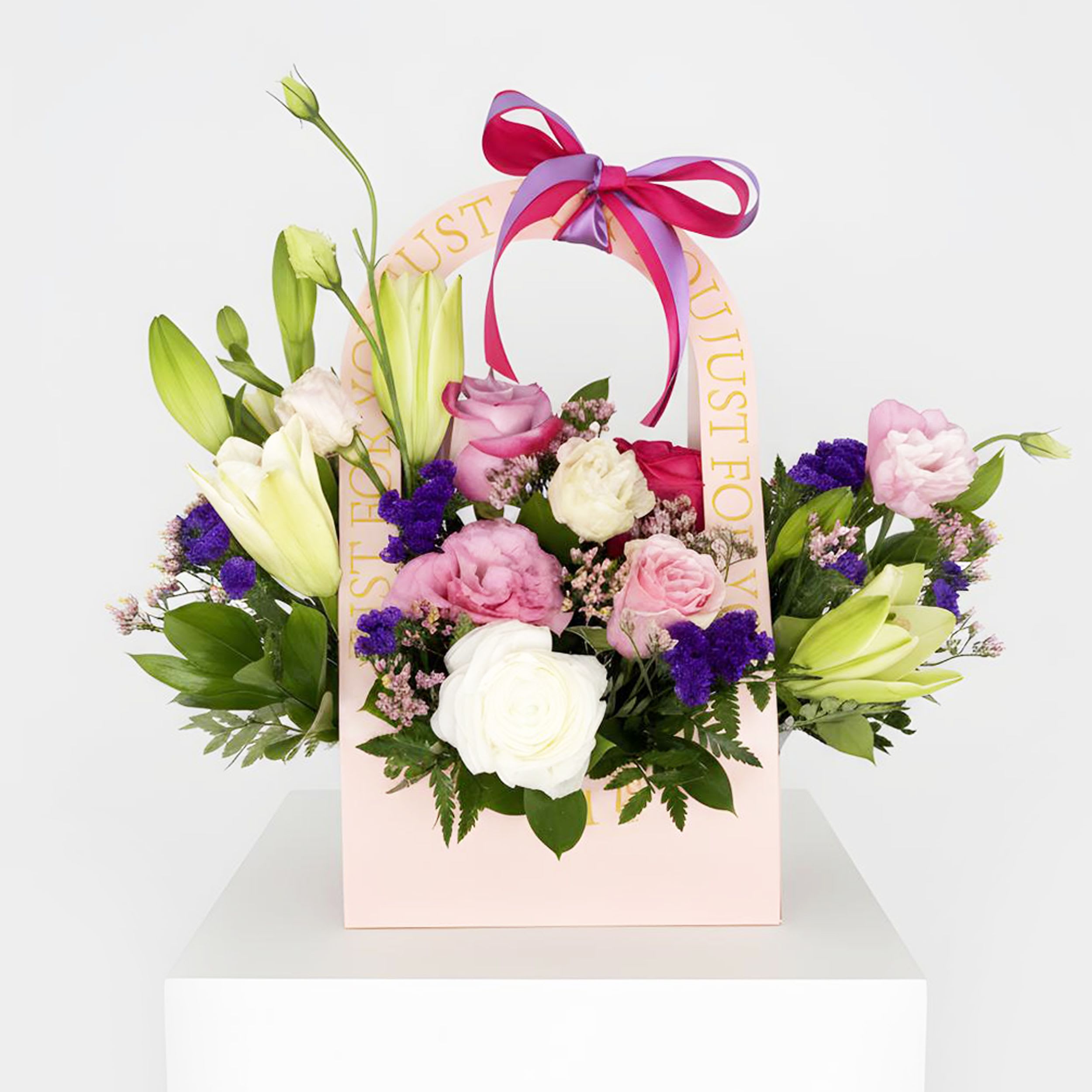 Just For You™ - A charming expression of love, appreciation, and thoughtful giving, Just For You™ Floral Purse is designed to make any recipient feel truly special. Arranged in an elegant keepsake purse-style container, this delightful design features a beautiful blend of white lilies, premium roses in shades of pink and white, delicate lisianthus, vibrant statice, and seasonal accent blooms nestled among fresh greenery. Finished with a stylish ribbon, this arrangement offers a perfect balance of sophistication and whimsy.  Whether celebrating a birthday, sending congratulations, expressing gratitude, or simply brightening someone's day, Just For You™ Floral Purse delivers beauty and joy in a memorable presentation.  Flower varieties and shades may vary based on seasonal availability while maintaining the overall style, color palette, and value of the arrangement.