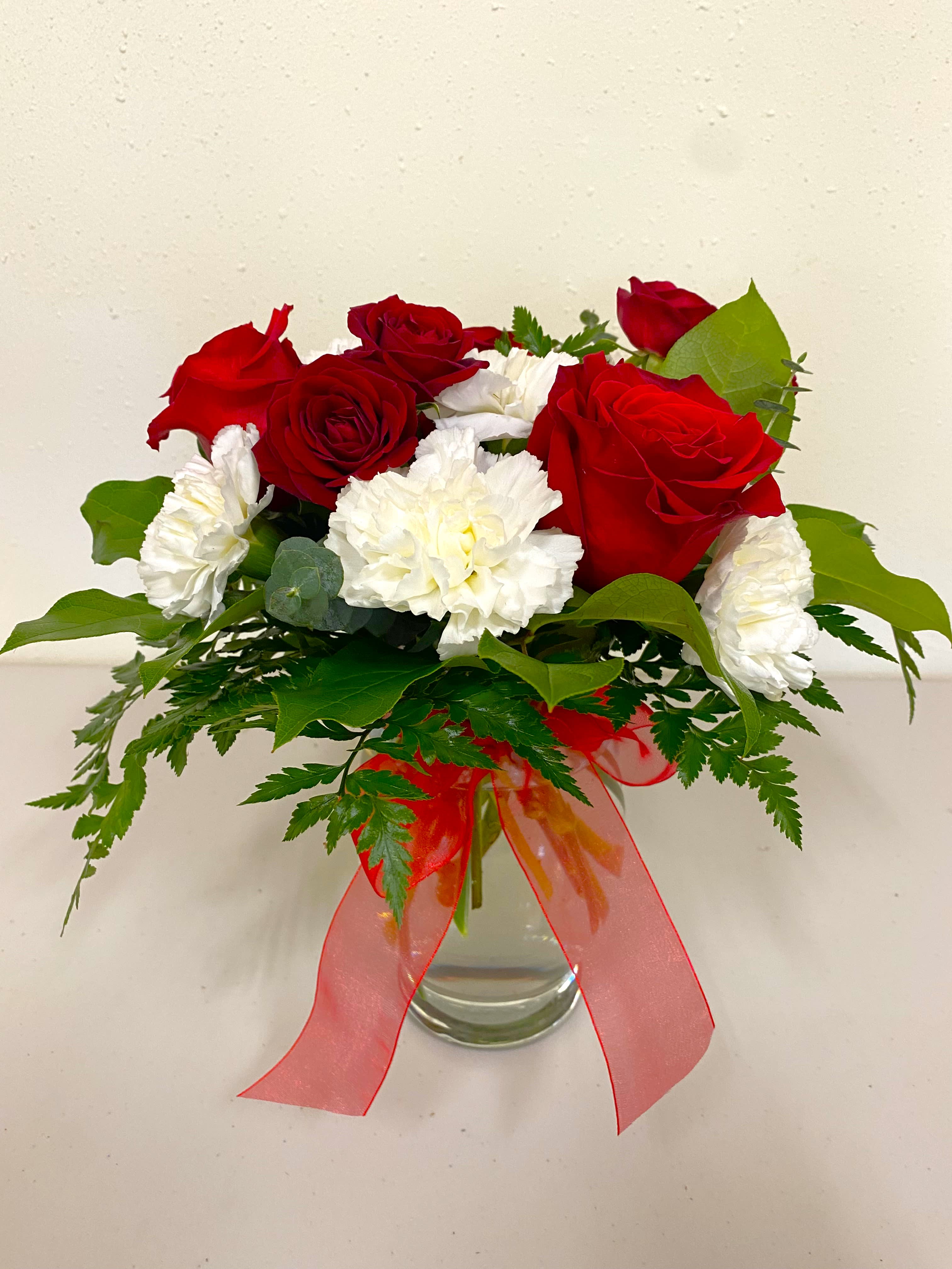 Red roses and white carnations in a glass vase with a red ribbon