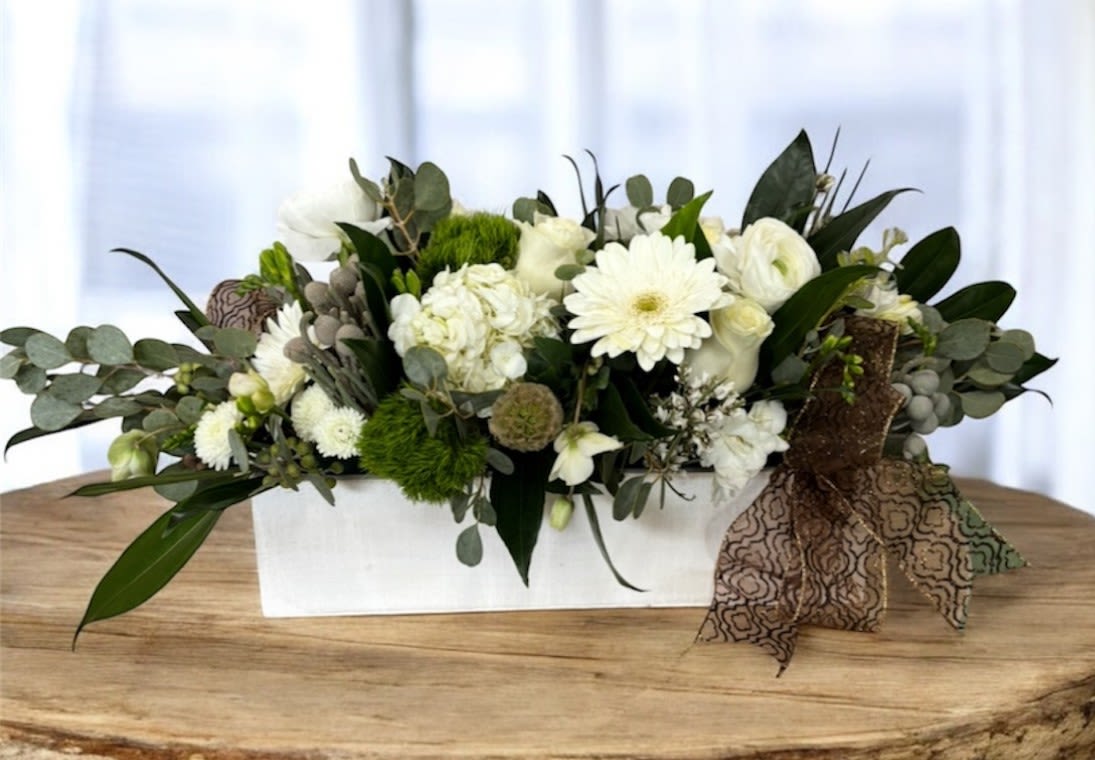 White floral arrangement in a rectangular white container with a patterned ribbon