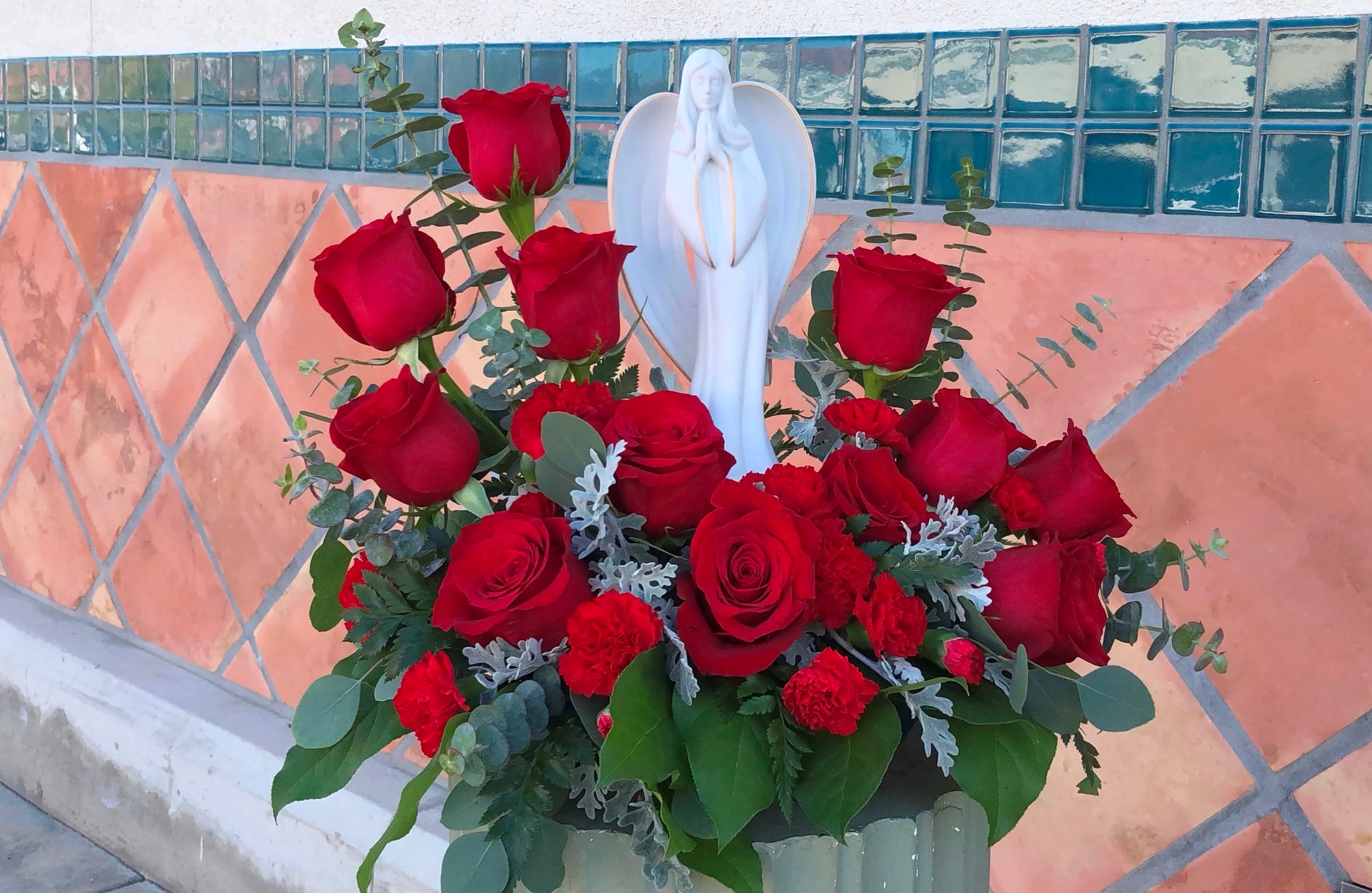 Red roses arranged around a white angel figurine in a vase