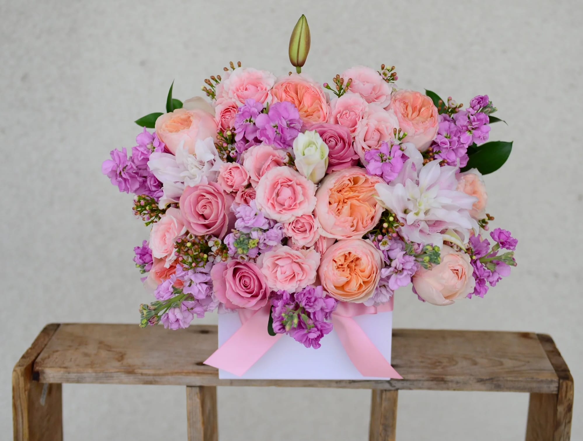 Pink and peach rose bouquet with purple blooms in a white box tied with ribbon