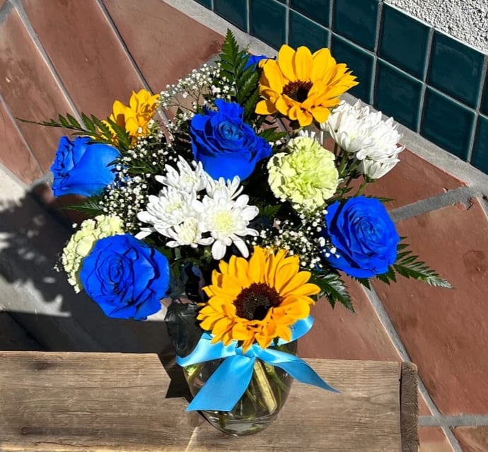 Bouquet of blue roses, sunflowers, and white daisies in a glass vase