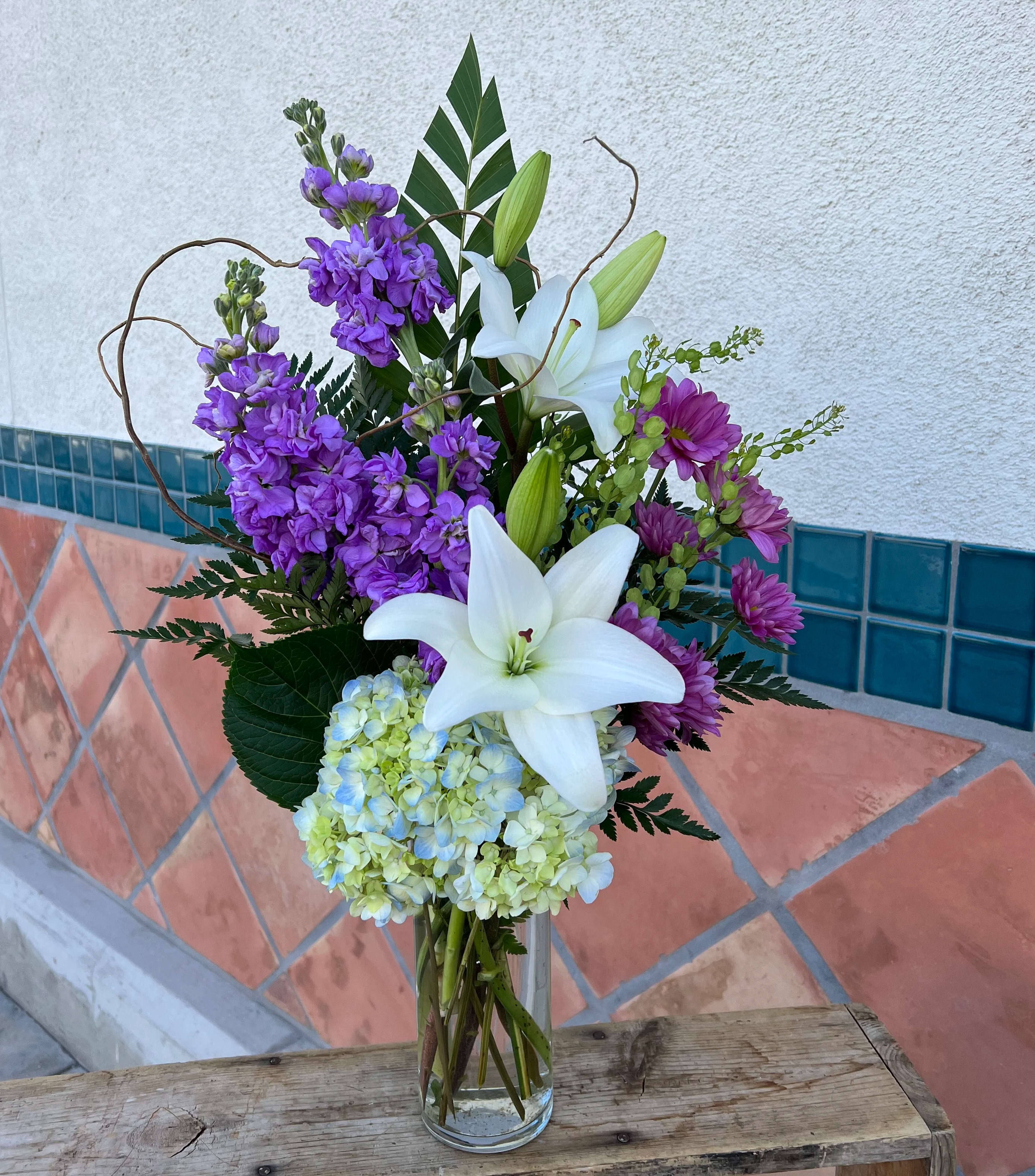 Purple flowers and white lilies arranged in a clear glass vase