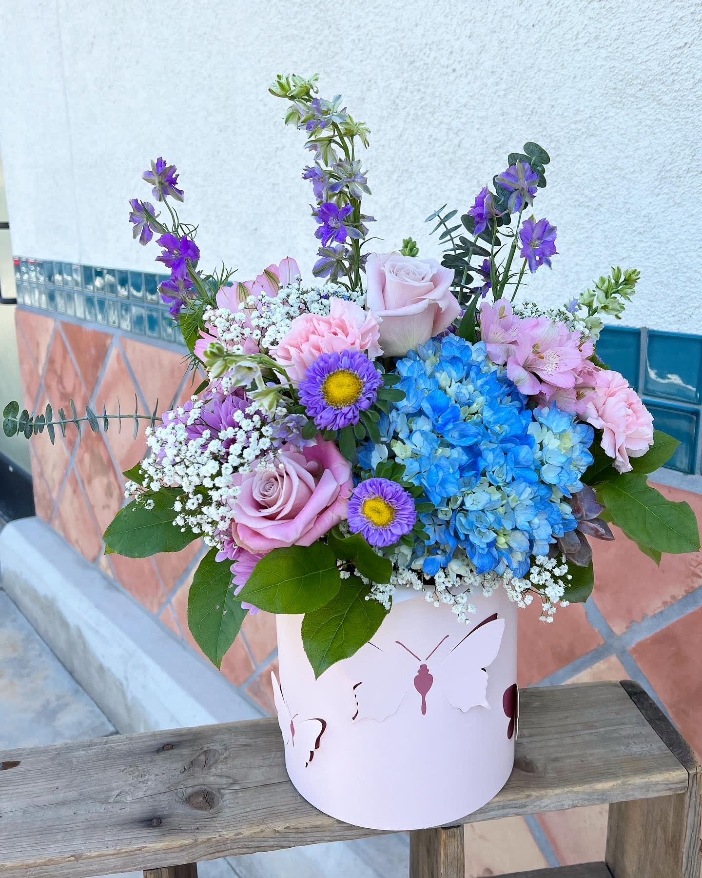Bouquet of pink roses, blue hydrangeas, and purple flowers in a pink butterfly box