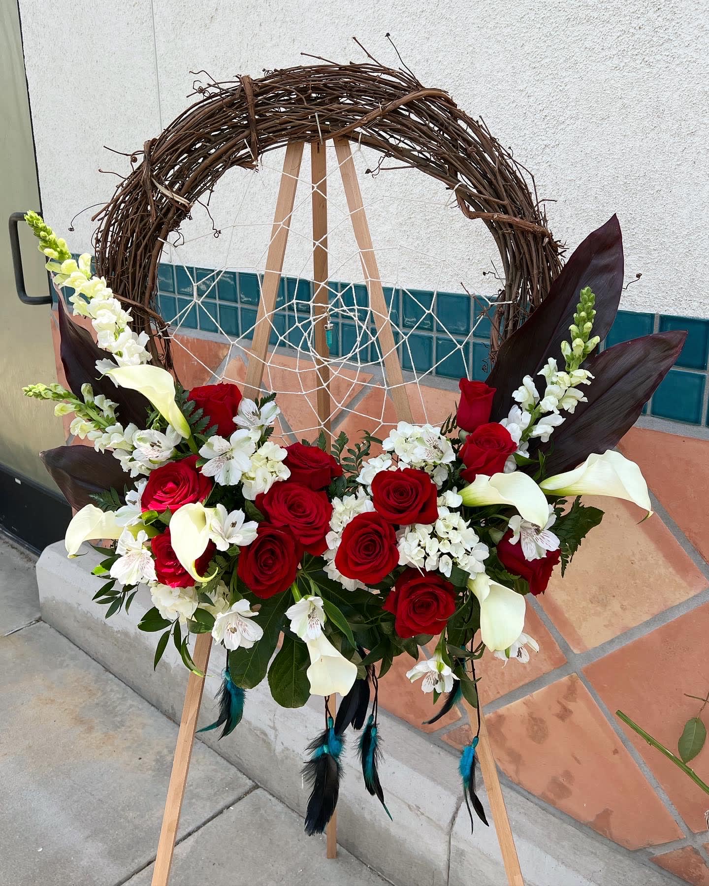 Floral wreath with red roses, white calla lilies, and white blossoms on an easel