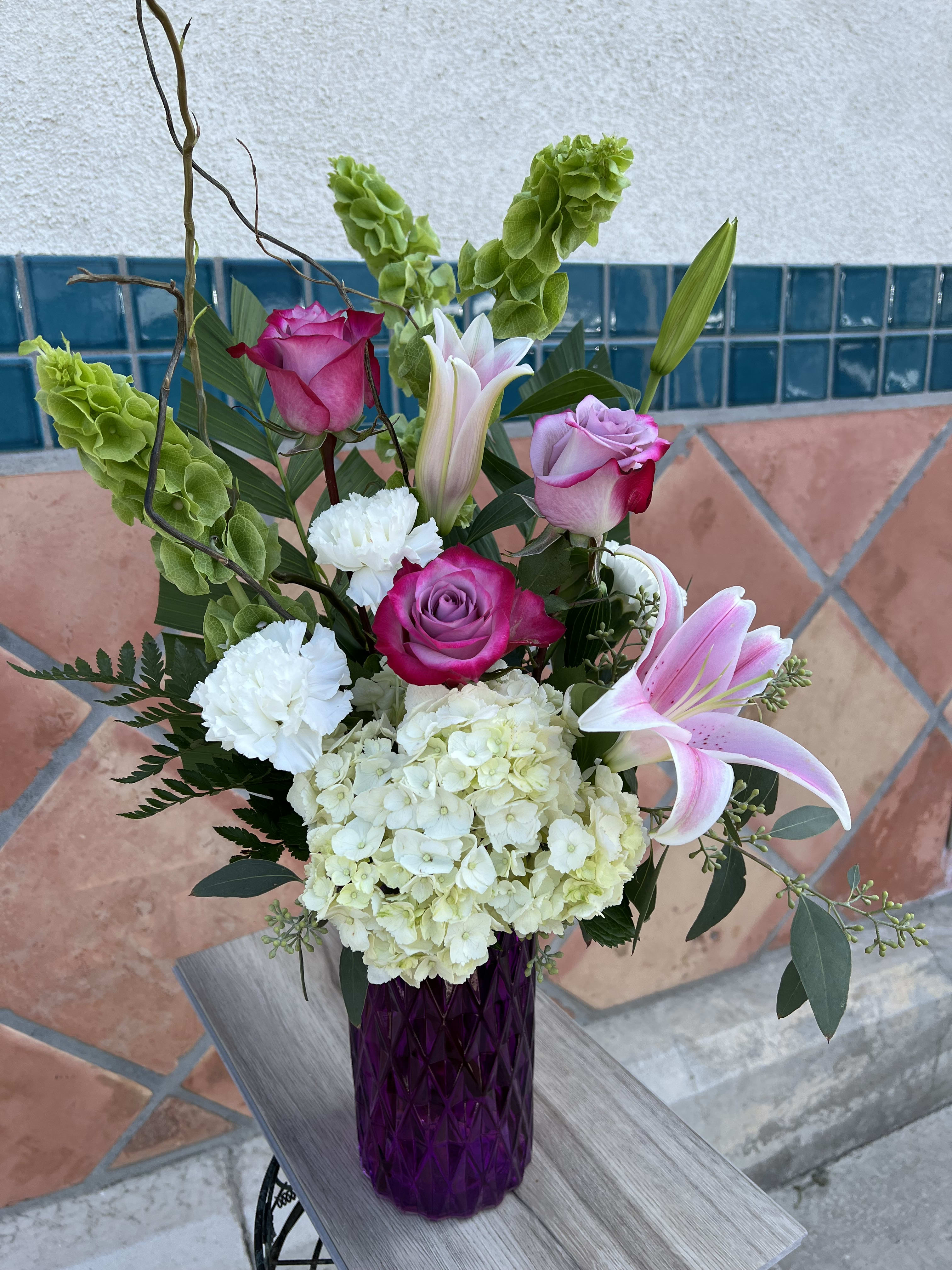 Amethyst bouquet  - pink, lavender, and purple flowers are artistically arranged inside an intricate diamond-cut pattern  glass vase.  