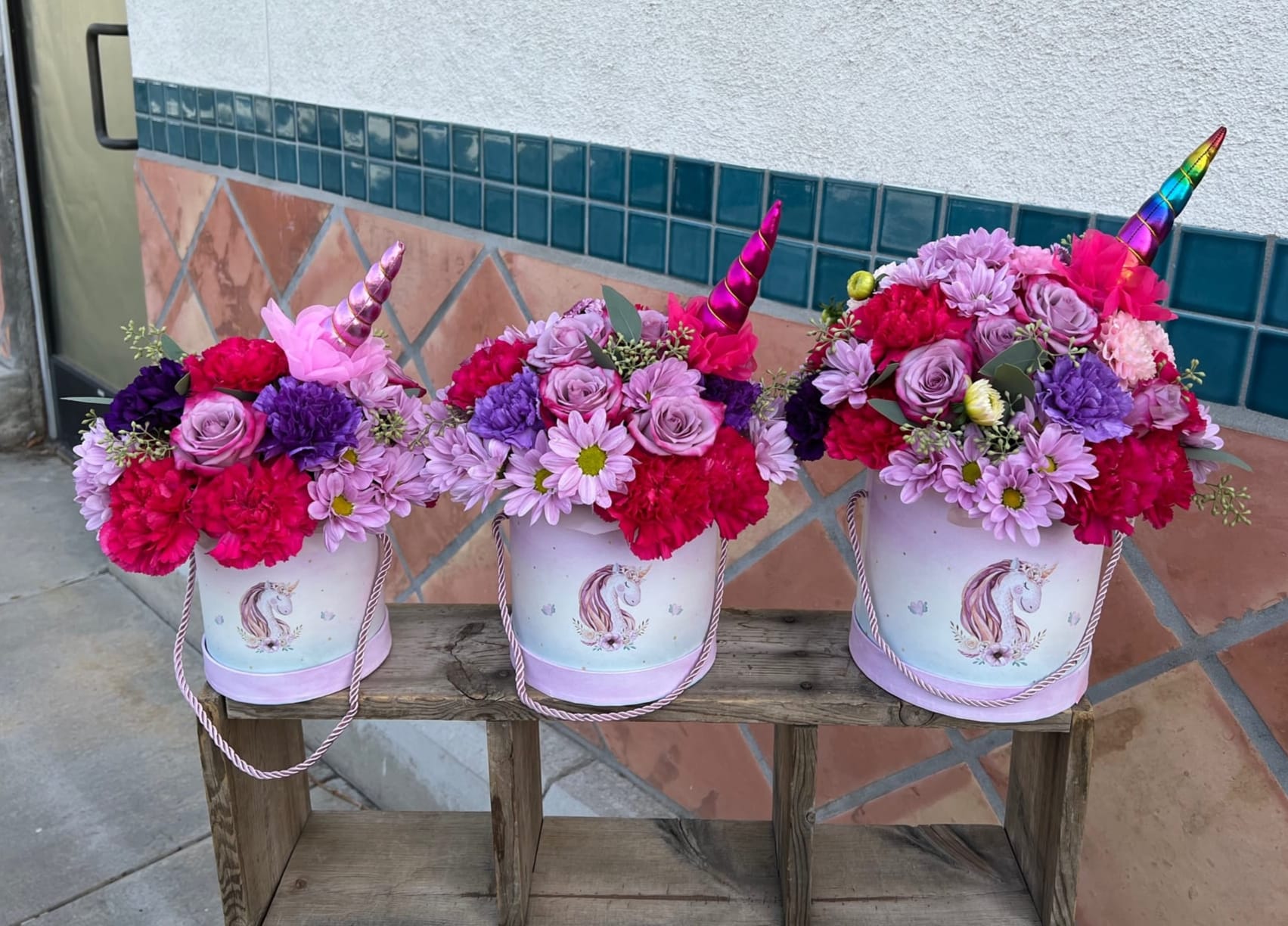 Three unicorn-themed flower buckets filled with pink and purple blooms