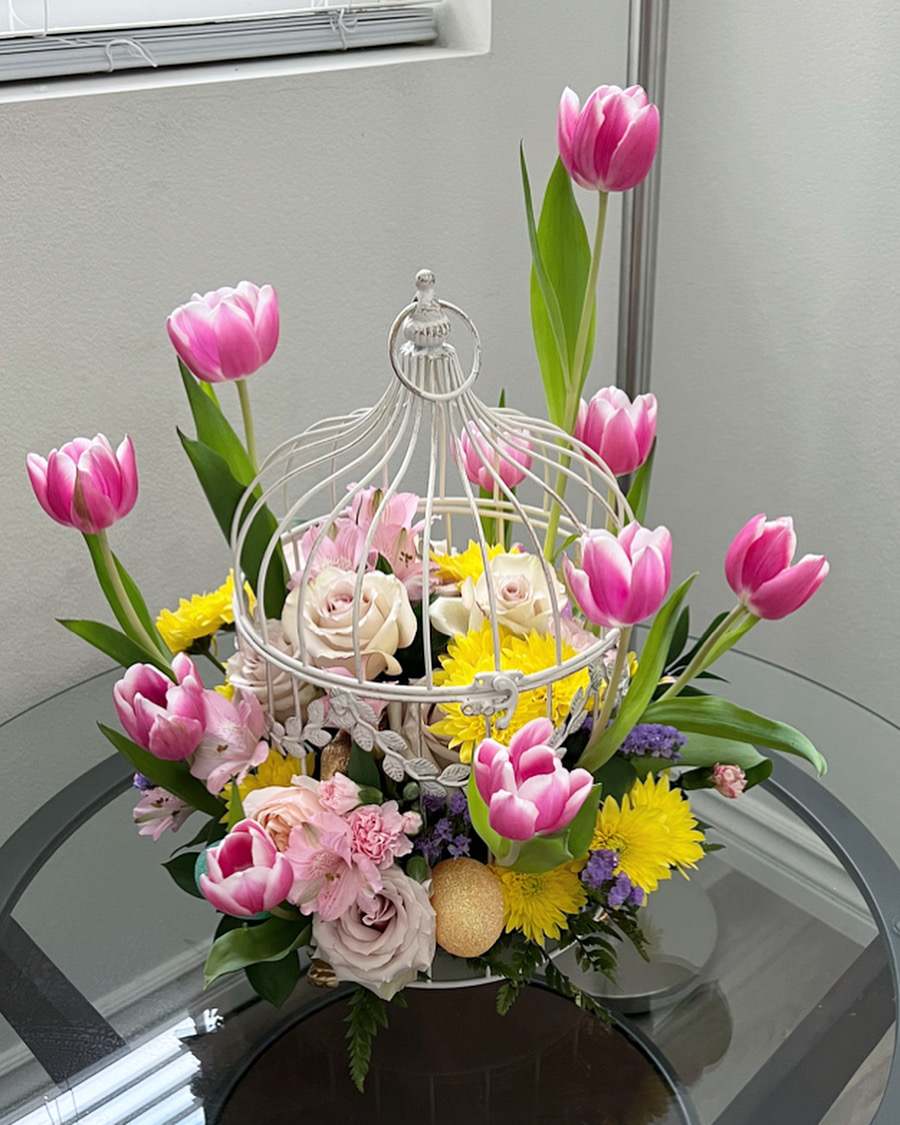 Pink tulips and mixed flowers arranged in a white birdcage centerpiece