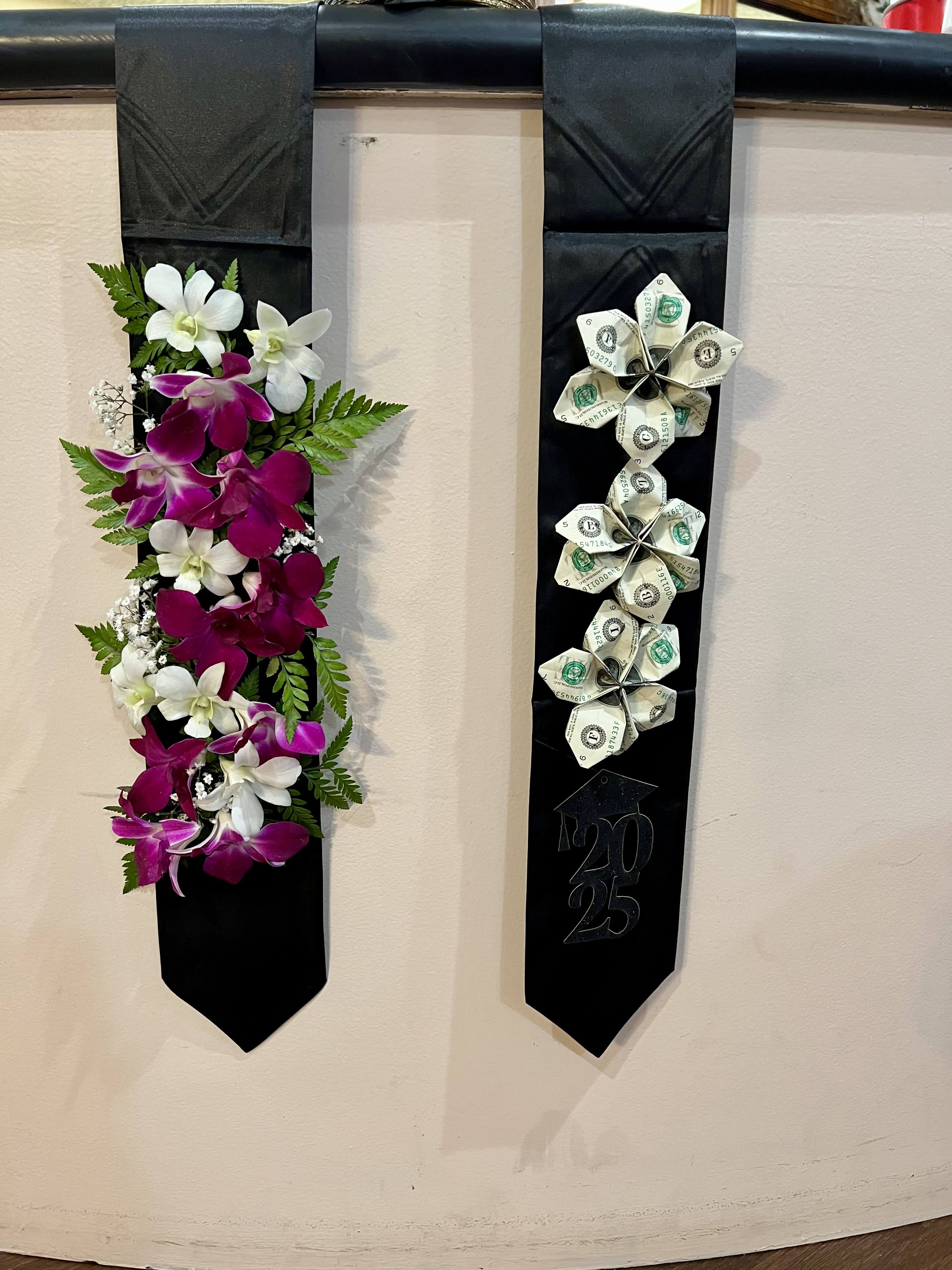 Two black graduation stoles, one with orchids and one with folded money flowers