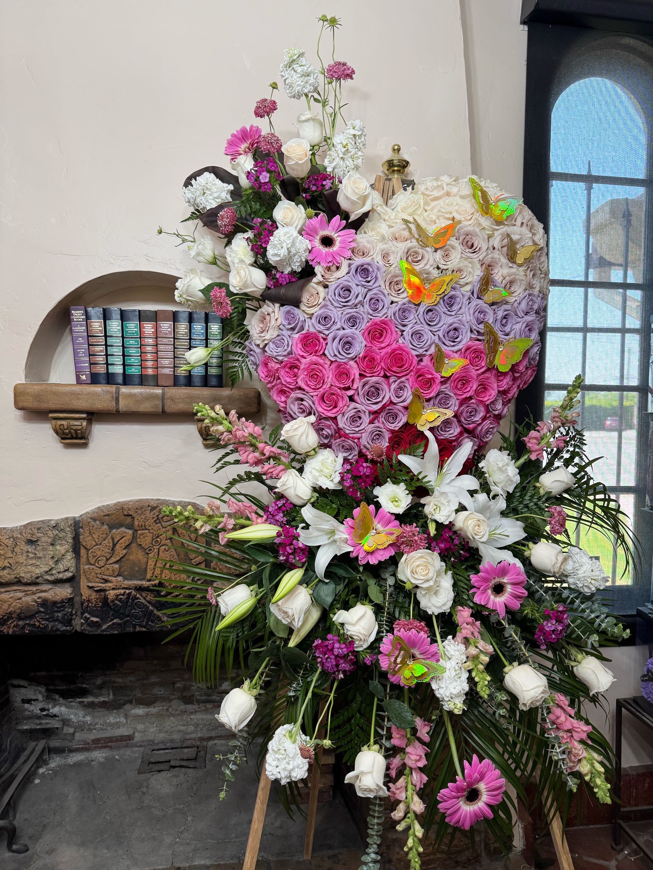 Ombré Rose Heart Spray - Celebrate a beautiful life with our Ombre heart-shaped standing spray. Featuring a stunning ombré of roses that gracefully shift from deep red to soft blush and ivory, this arrangement symbolizes the journey of love, remembrance, and peace. Expertly designed in a lush heart shape and displayed on a standing easel, it’s a touching tribute that brings warmth and beauty to any memorial or funeral service.