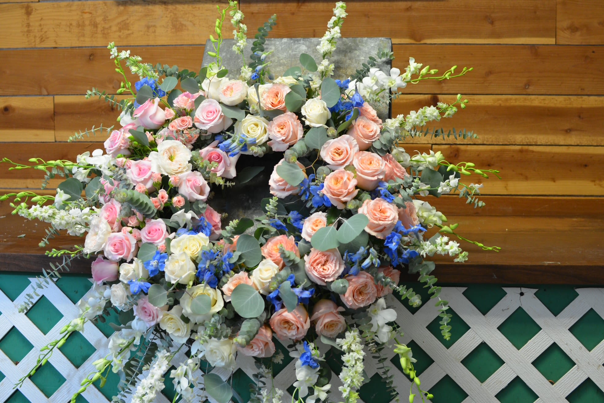 Pastel Wreath - Celebrate life's special moments with the timeless beauty of our Pastel Wreath. Designed in a soothing palette of soft pastel tones, this elegant wreath features delicate roses, graceful dendrobium orchids, airy delphinium, and fragrant eucalyptus. The combination of lush blooms and fresh greenery creates a gentle, serene arrangement that expresses love, remembrance, and heartfelt sympathy.  Handcrafted with care, the Pastel Wreath offers a refined and comforting tribute, making it a meaningful choice for memorial services, funerals, or celebrations of life. Its soft colors and natural elegance convey peace, hope, and everlasting affection.