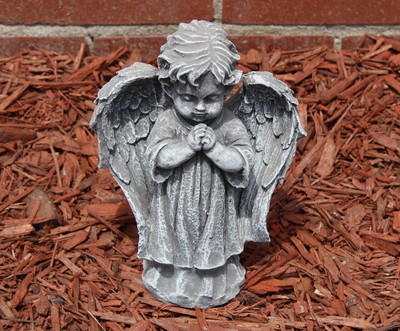 Small gray angel statue with folded hands in mulch