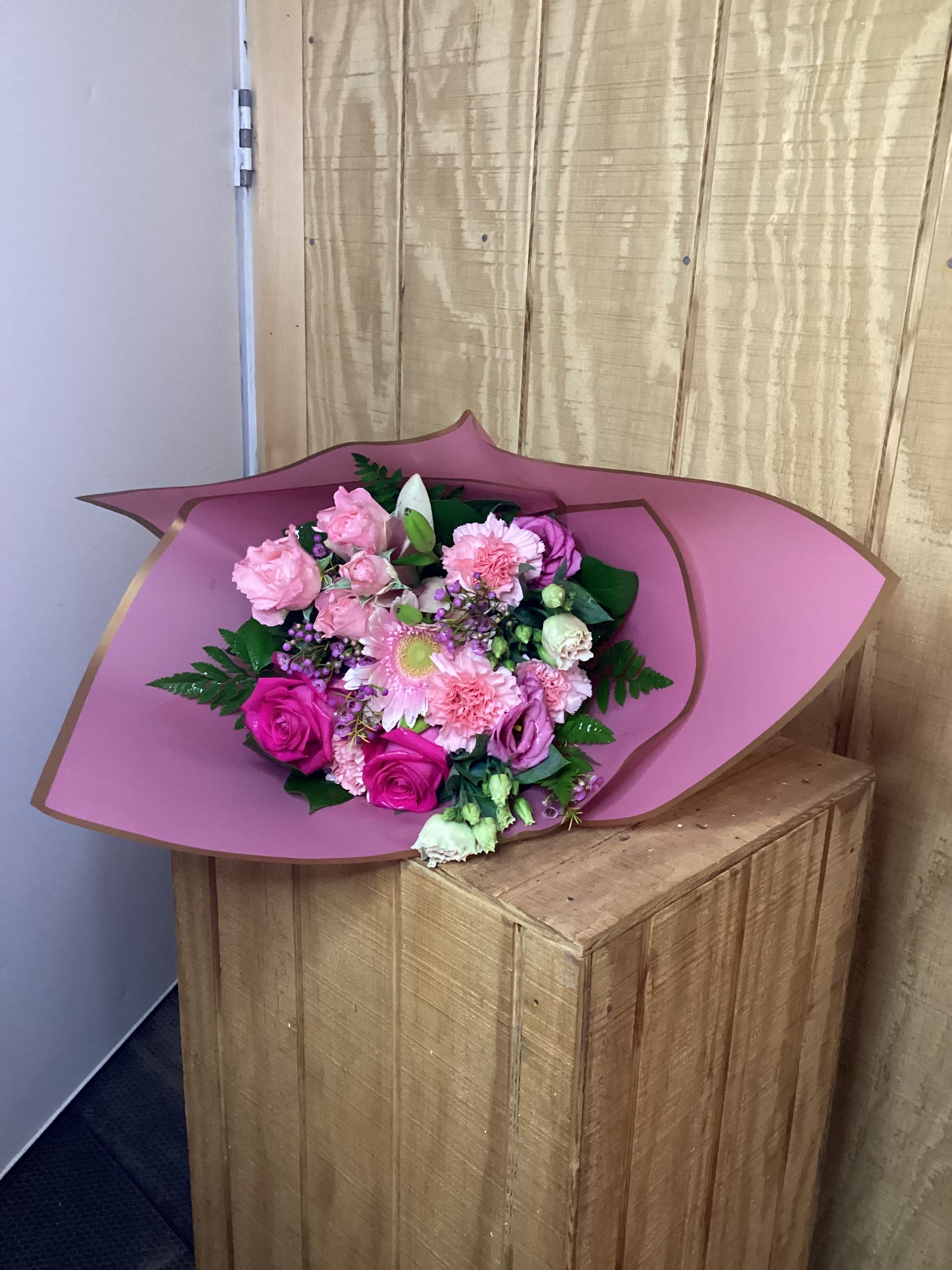 Pink bouquet with roses, carnations, and a daisy-like bloom wrapped in mauve paper