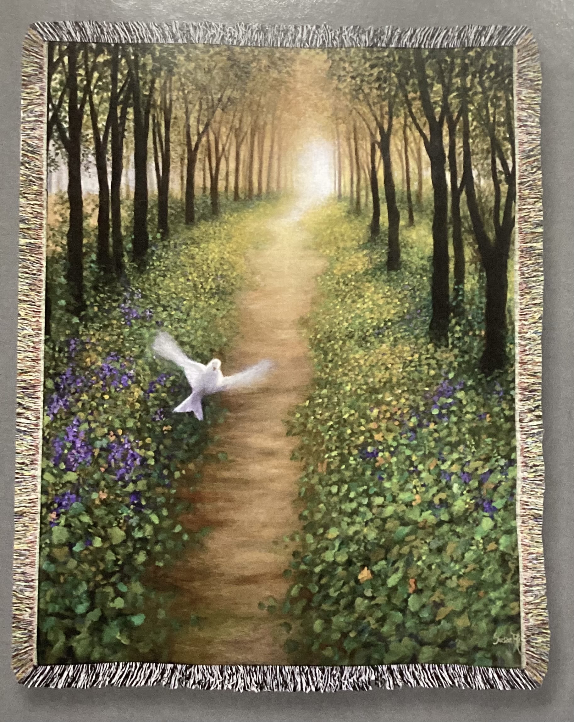 Fringed wall tapestry showing a forest path with a white dove