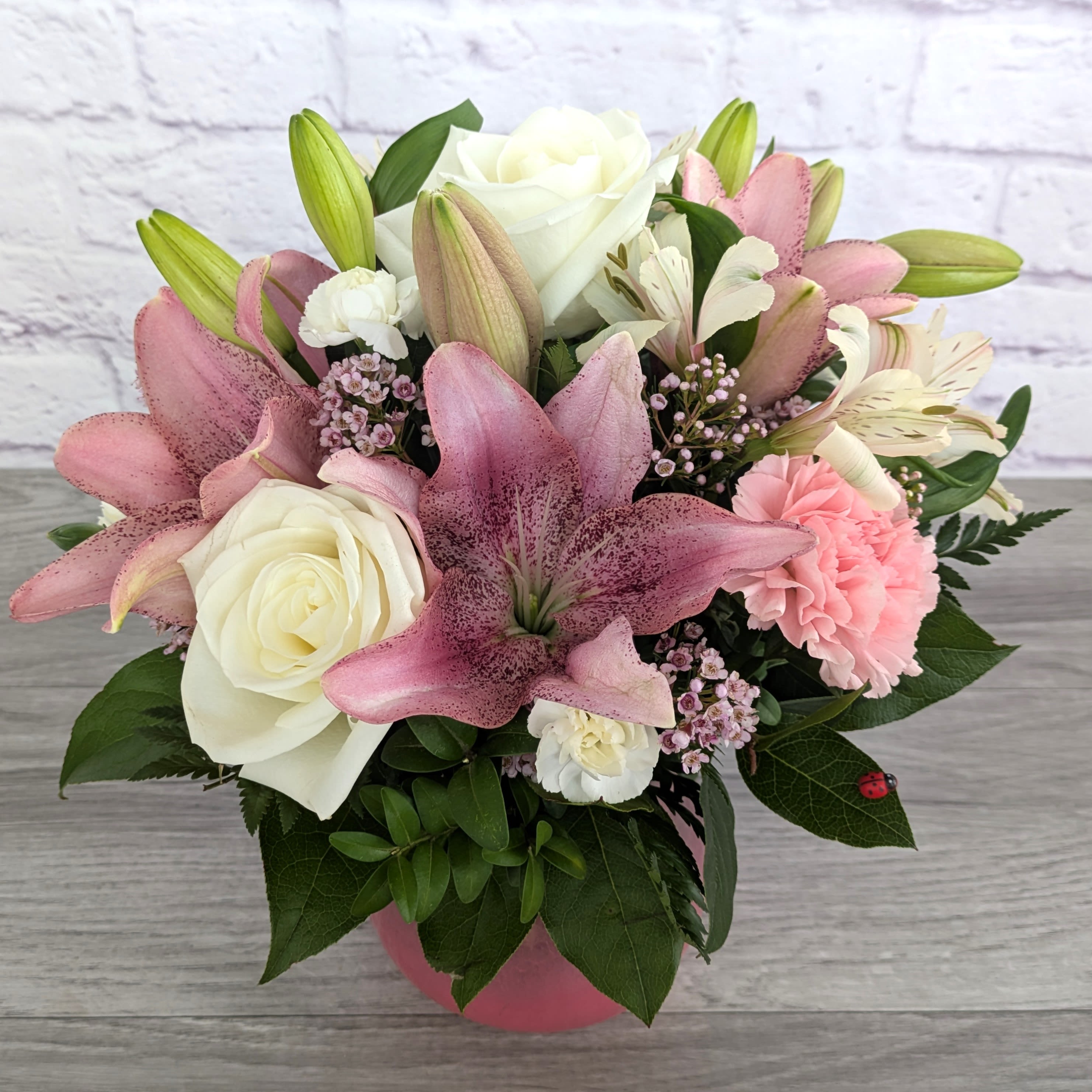 Poised In Pink - Poised In Pink is A Ladybug Floral exclusive bouquet.. This bouquet includes Asiatic lilies, roses, carnations, alstromeria, mini carnations and wax flower. Featured in a translucent crackled glass vase with a pink gradient.  Orientation: All Around 14” Tall 14” Wide  