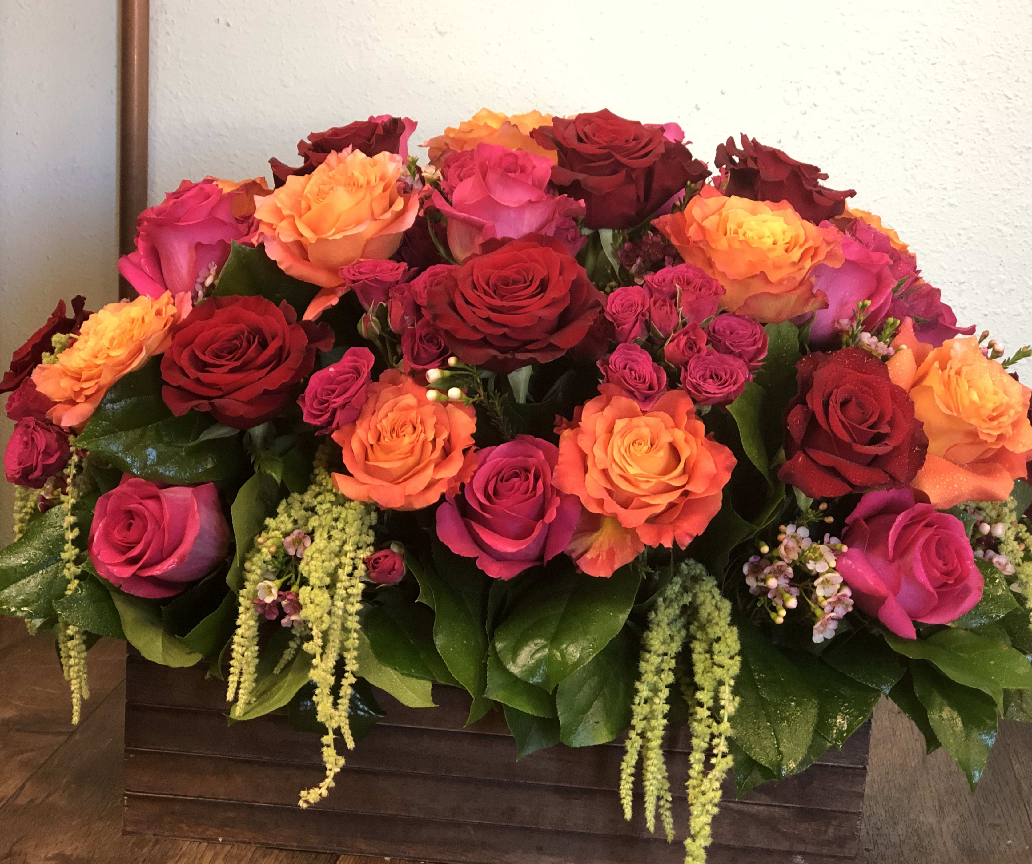 Low rectangular arrangement of red, orange, and hot pink roses in a wooden box