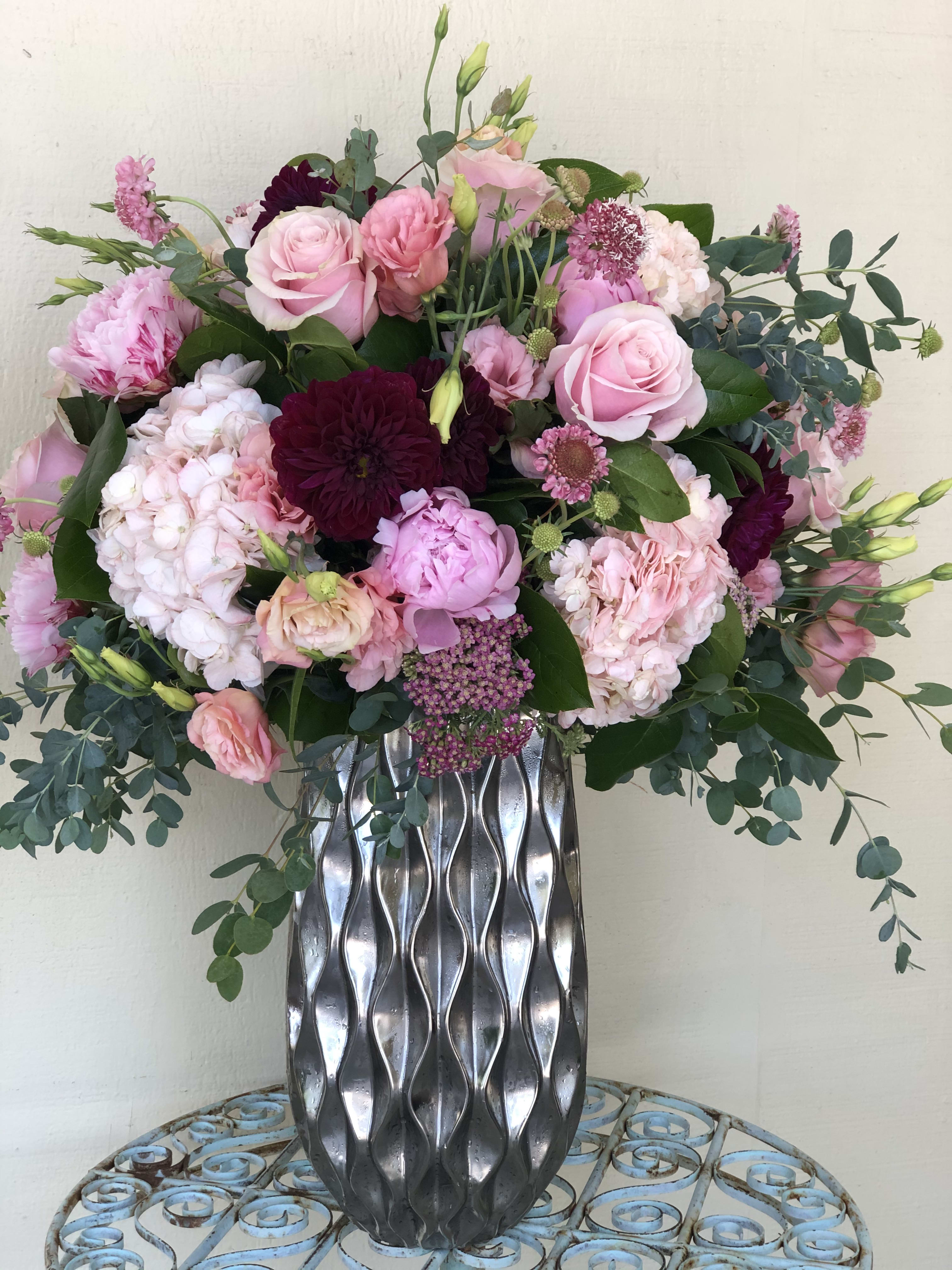 Tall arrangement of pink and burgundy flowers in a silver textured vase