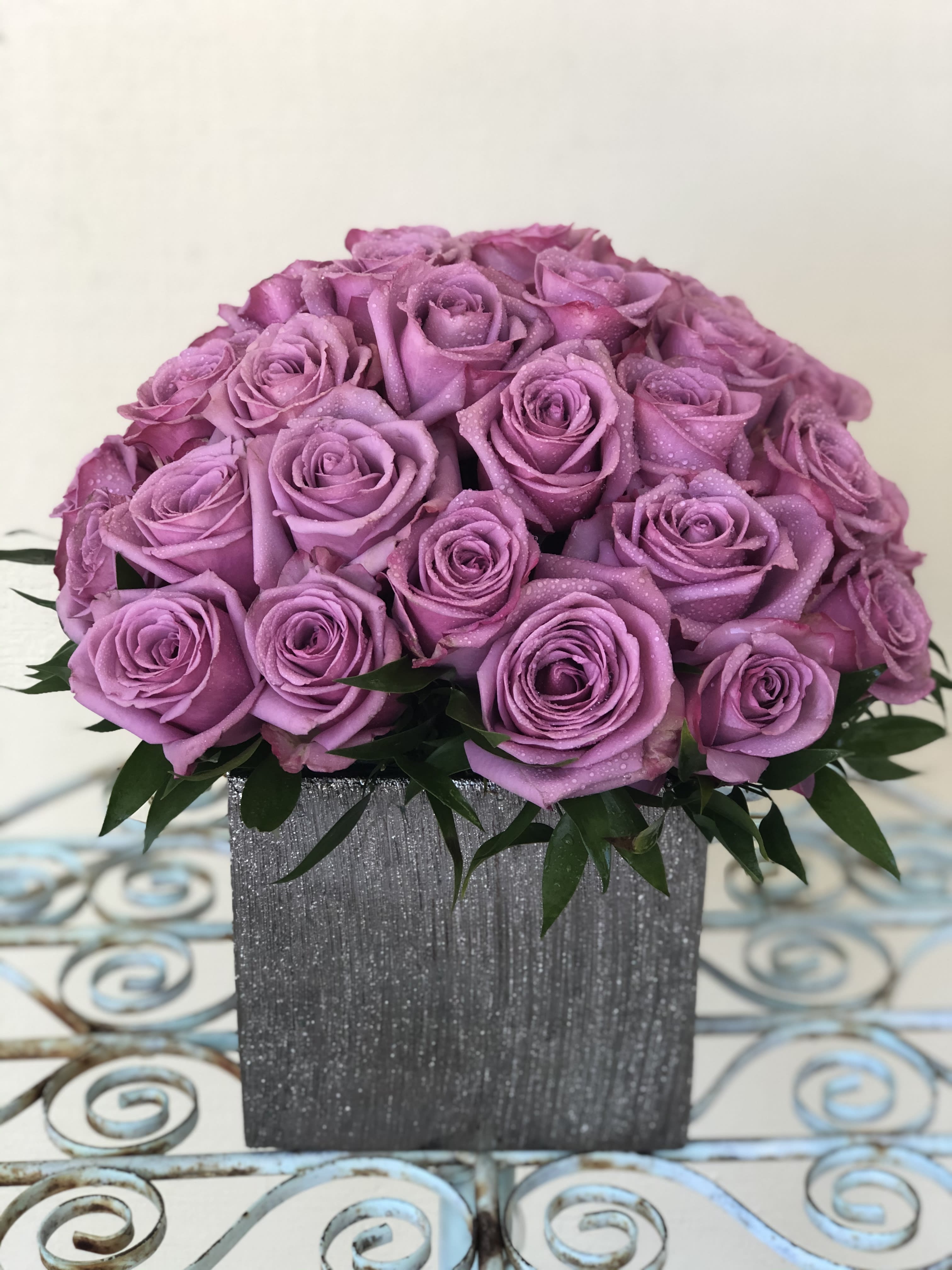 Lavender rose arrangement in a gray textured square vase on a decorative metal table