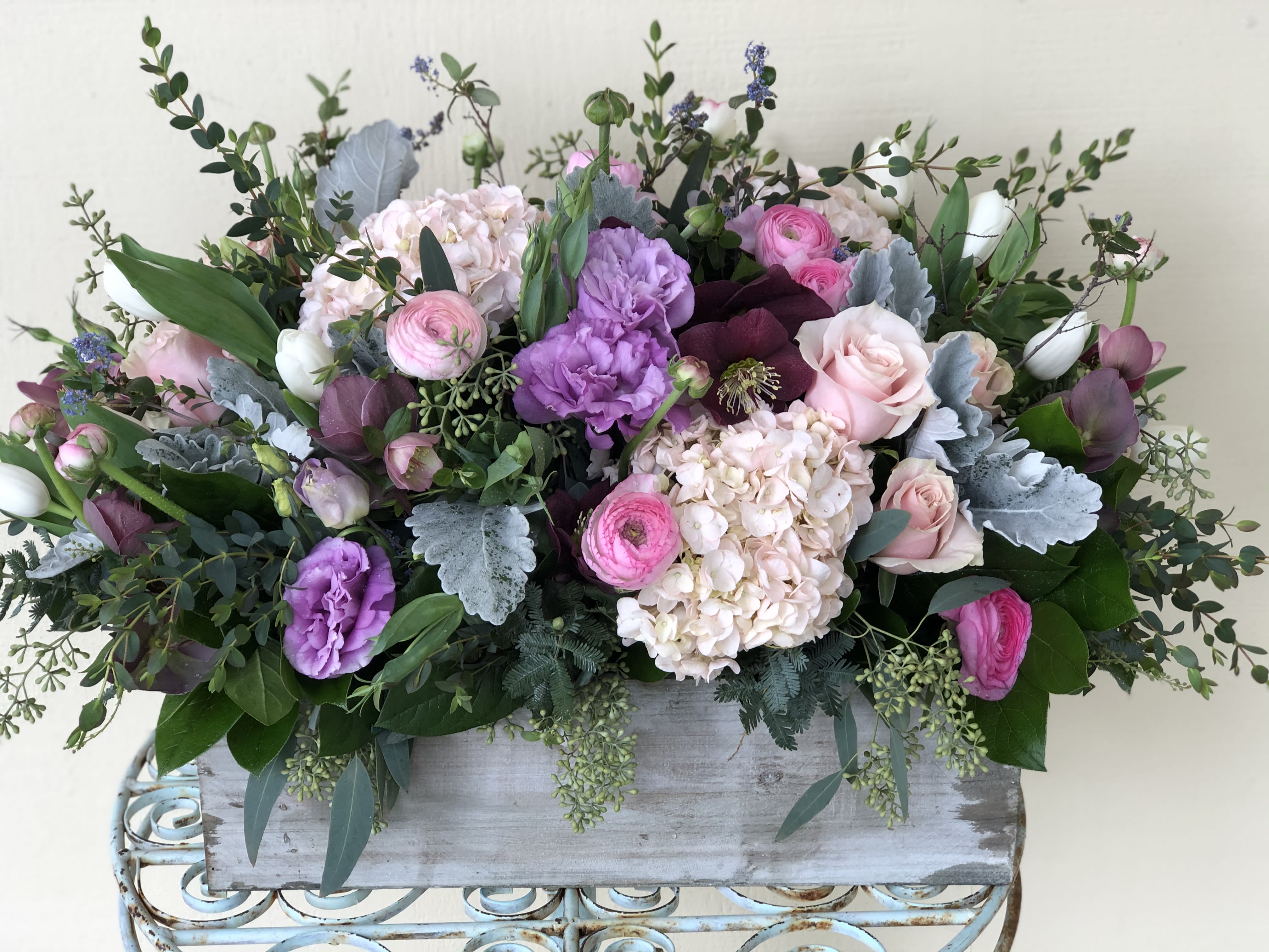 Low pastel arrangement of pink and purple flowers in a rustic rectangular wooden box