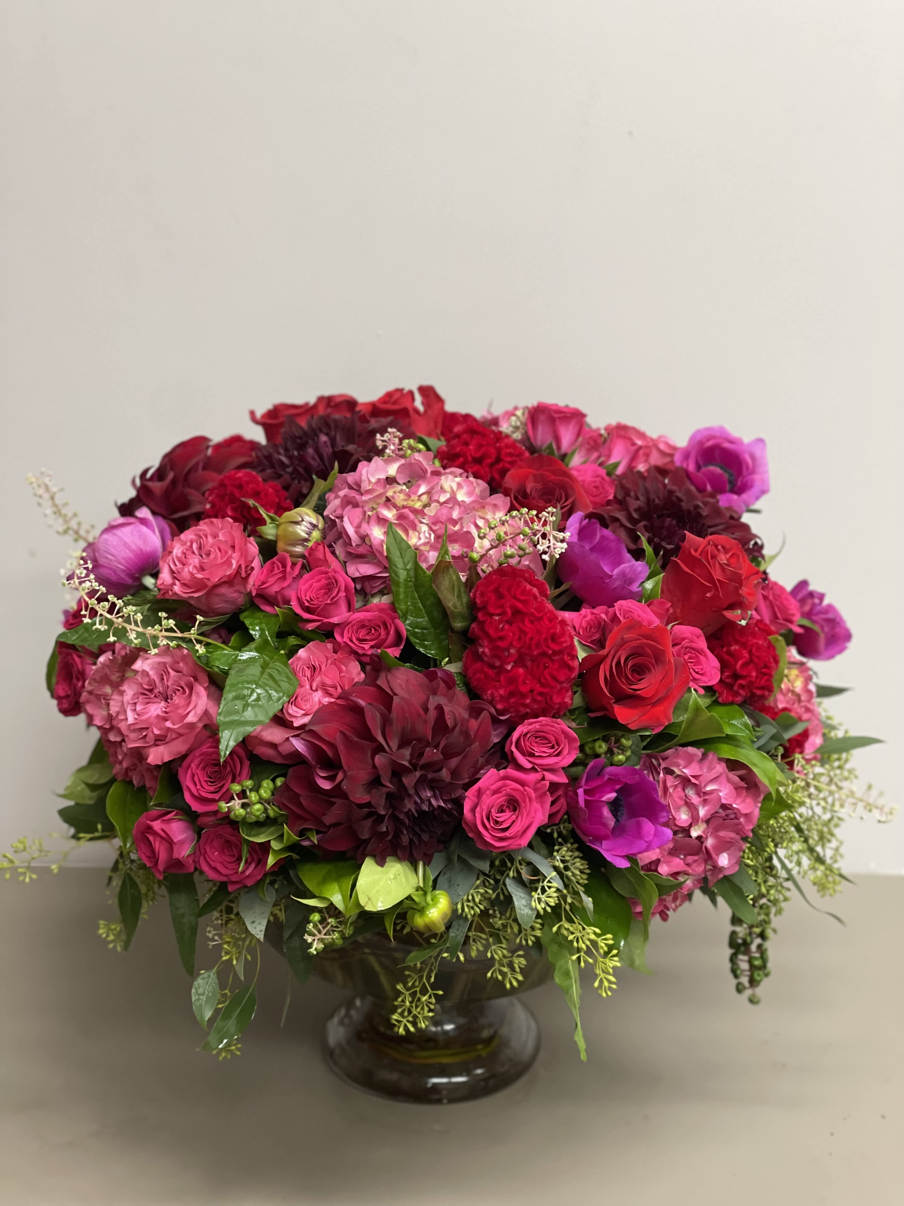 Low, lush arrangement of red and pink flowers in a clear glass pedestal bowl