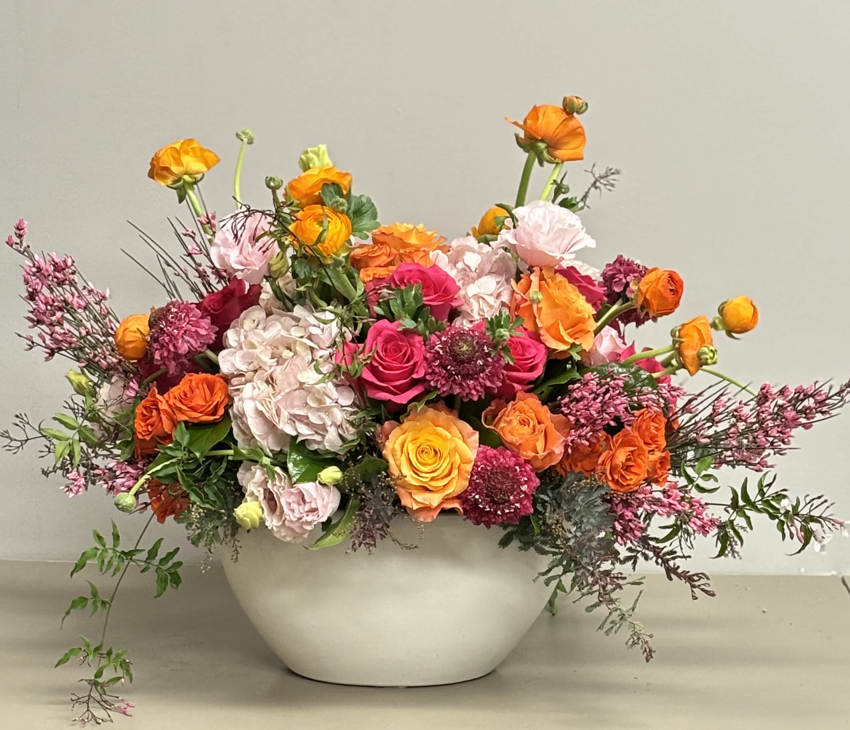 Low centerpiece of bright orange and pink flowers with pale hydrangea in a round white bowl