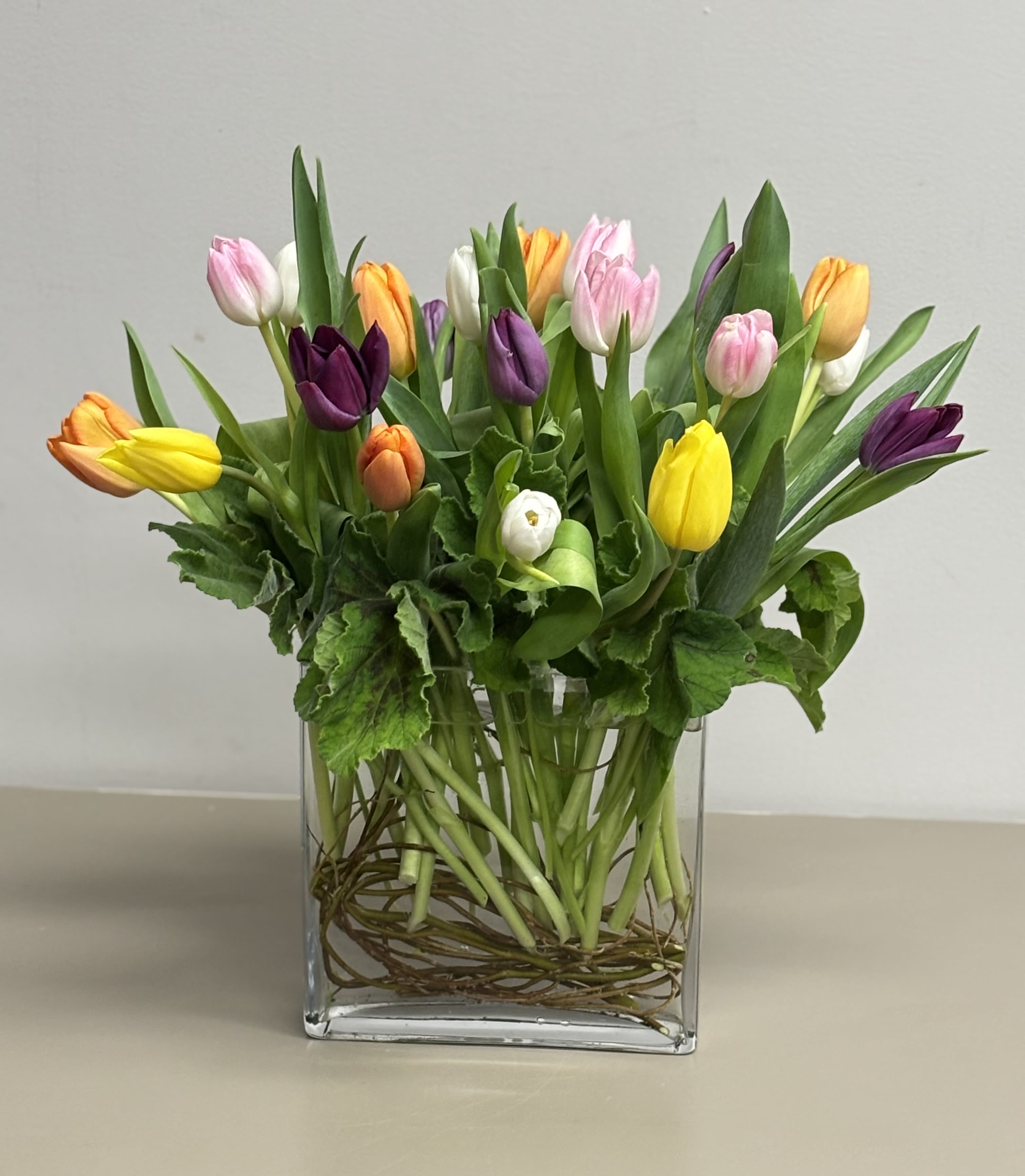 Mixed tulips in pink, yellow, purple, orange, and white in a clear glass vase