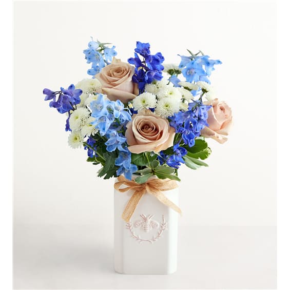 Bouquet of peach roses, blue flowers, and white blooms in a white vase