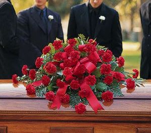 Red carnation casket spray with ribbon on a wooden casket