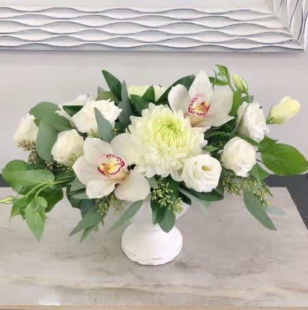 White floral arrangement in a white vase with orchids and chrysanthemums