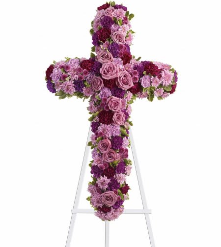 Tall floral cross of pink and purple blooms displayed on a white easel stand