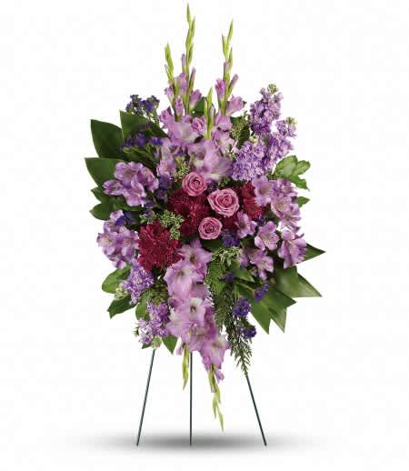 Tall standing spray of purple and pink flowers with roses, gladiolus, and stock on a green leaf backdrop.