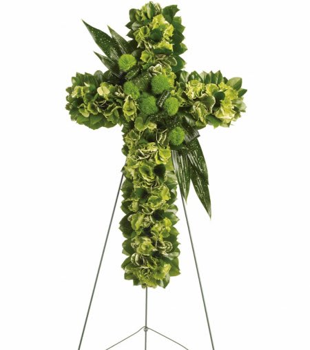 Green floral cross on a metal easel stand with clustered blooms and glossy leaf accents.