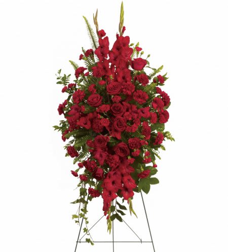 Tall standing spray of red roses and carnations with other red flowers on a metal easel.