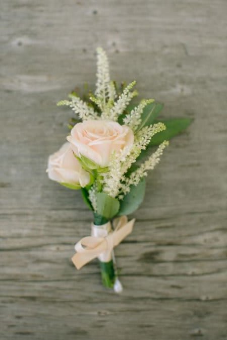 Blush rose wedding boutonniere with white filler flowers and an ivory ribbon bow.