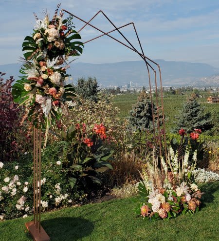 Tall geometric metal arch decorated with peach and white flowers in a garden setting