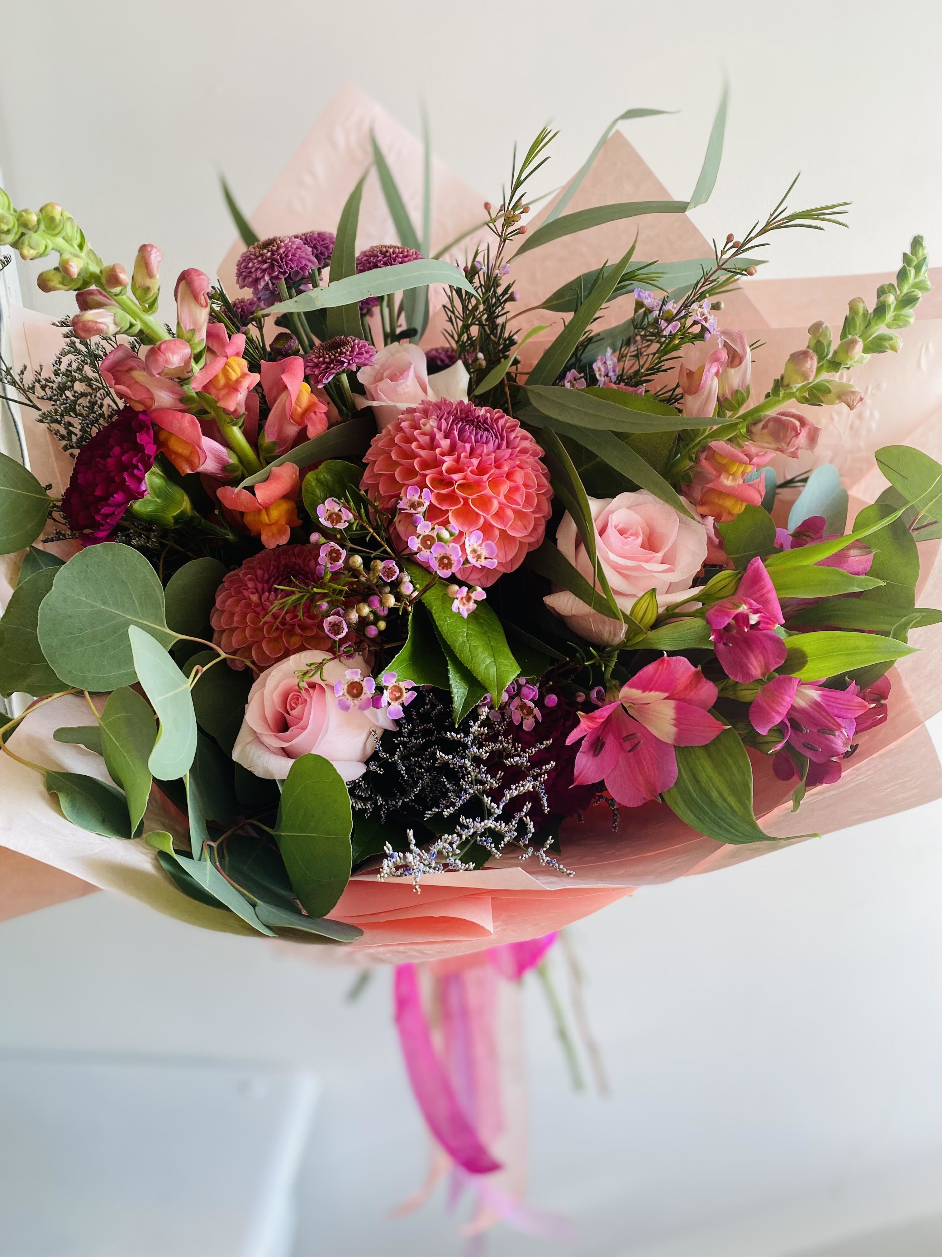 Bouquet of pink roses, dahlias, and snapdragons wrapped in pink paper