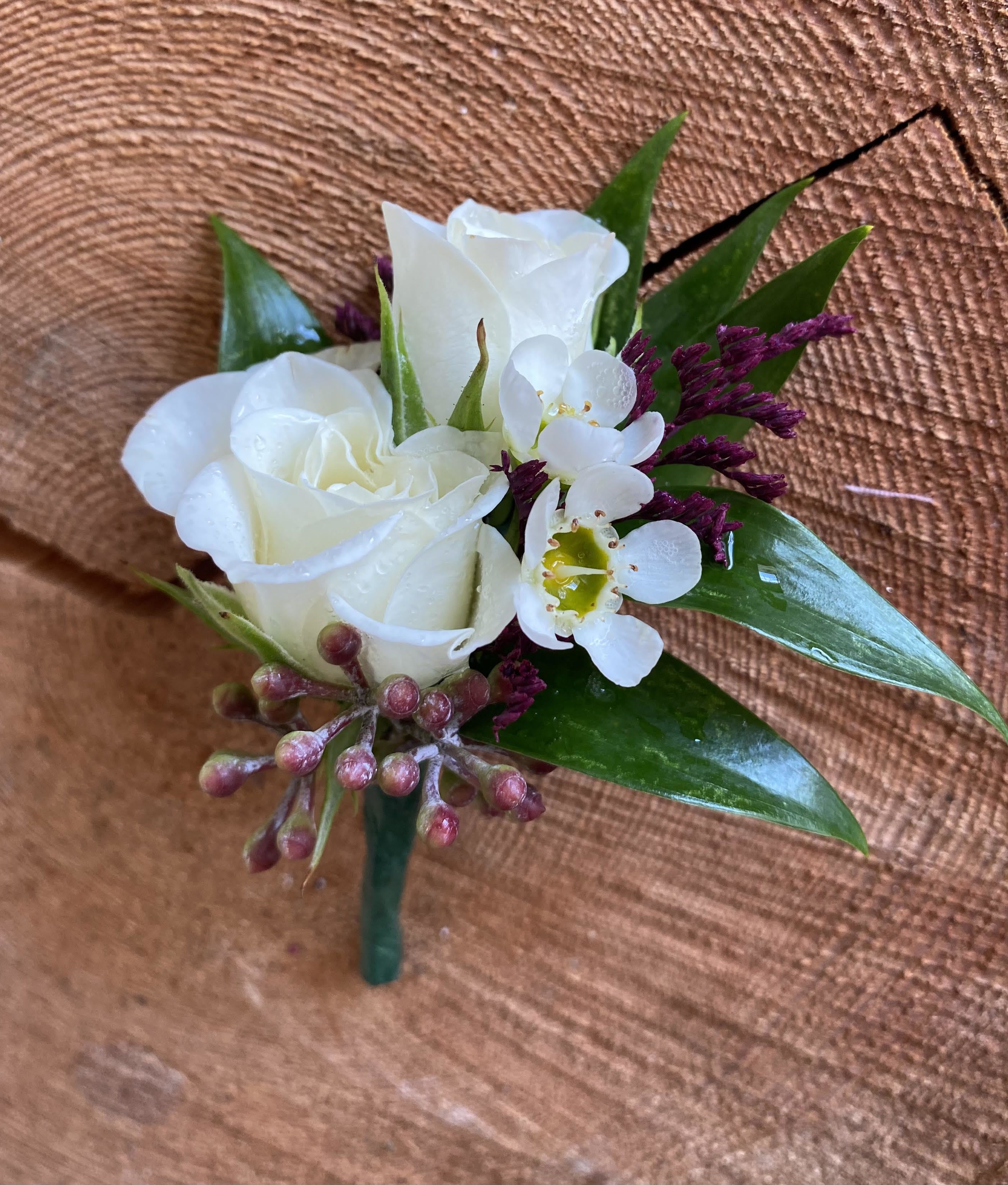 White rose boutonniere with purple accents and glossy leaves