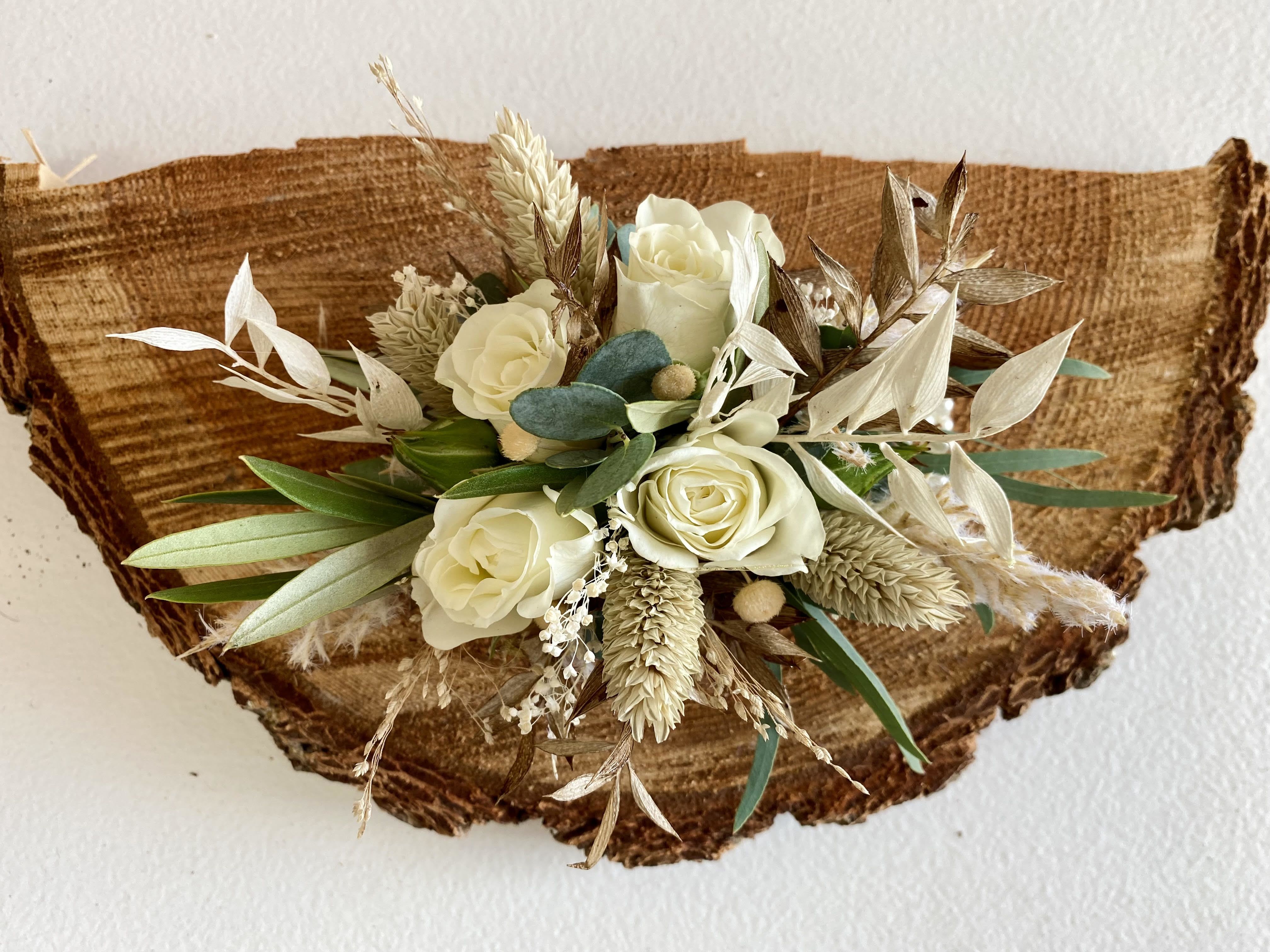 Cream roses with dried grasses in a compact arrangement on a rustic wood slice