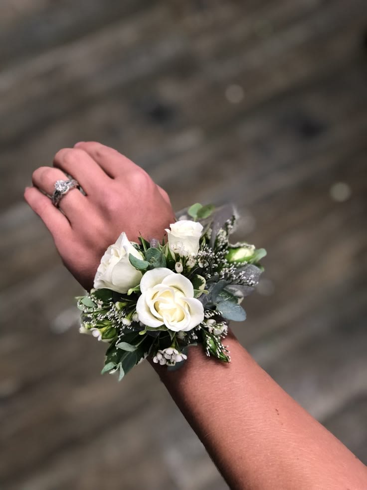 White rose wrist corsage with small white filler flowers worn on a wrist.