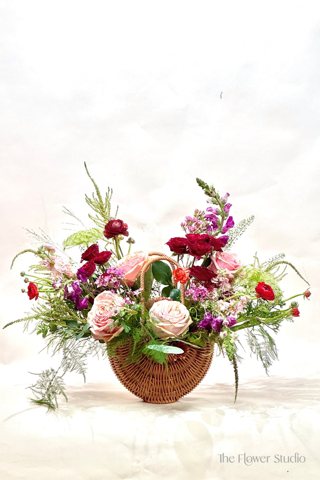 Basket arrangement of pink and red roses with purple flowers