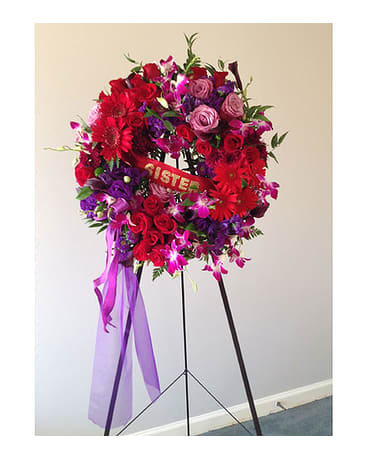 Large red and purple floral wreath on a stand with ribbon