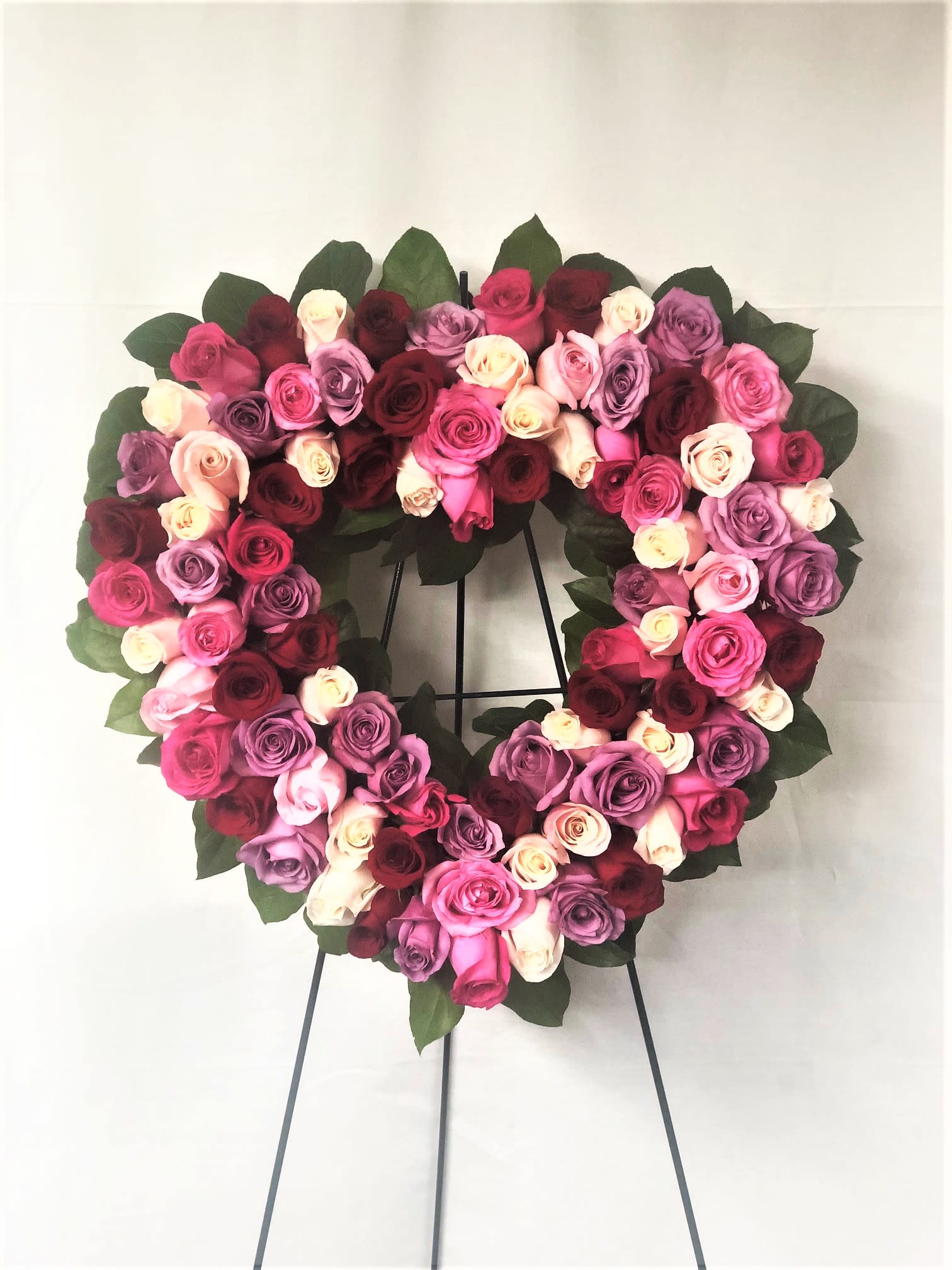 Heart-shaped wreath of pink, lavender, white, and red roses on a stand